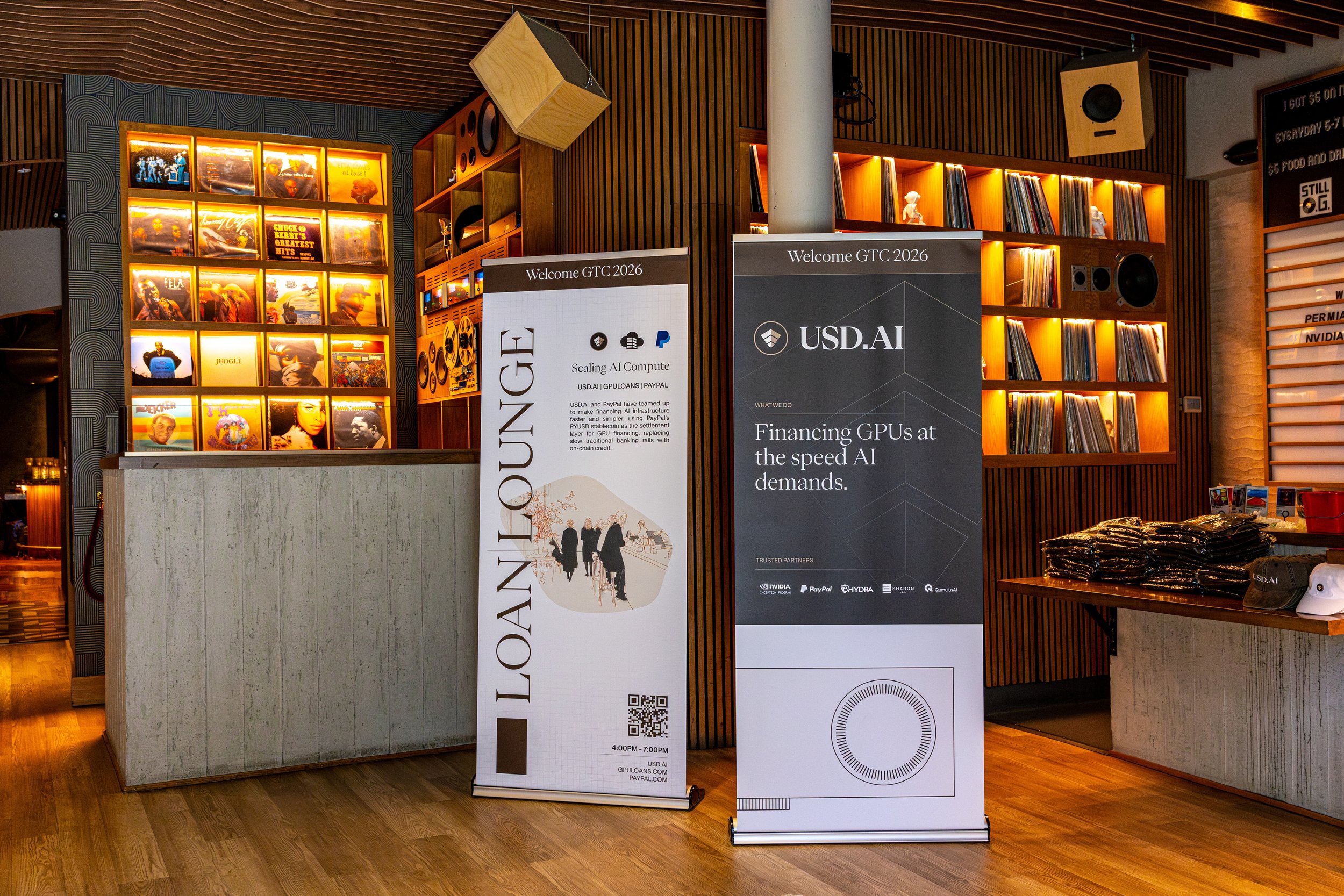 Interior of an event space featuring vinyl record displays, wooden shelving, and signage for USD AI at the GTC 2026 conference, with promotional materials and a wall of records illuminated with warm lighting.