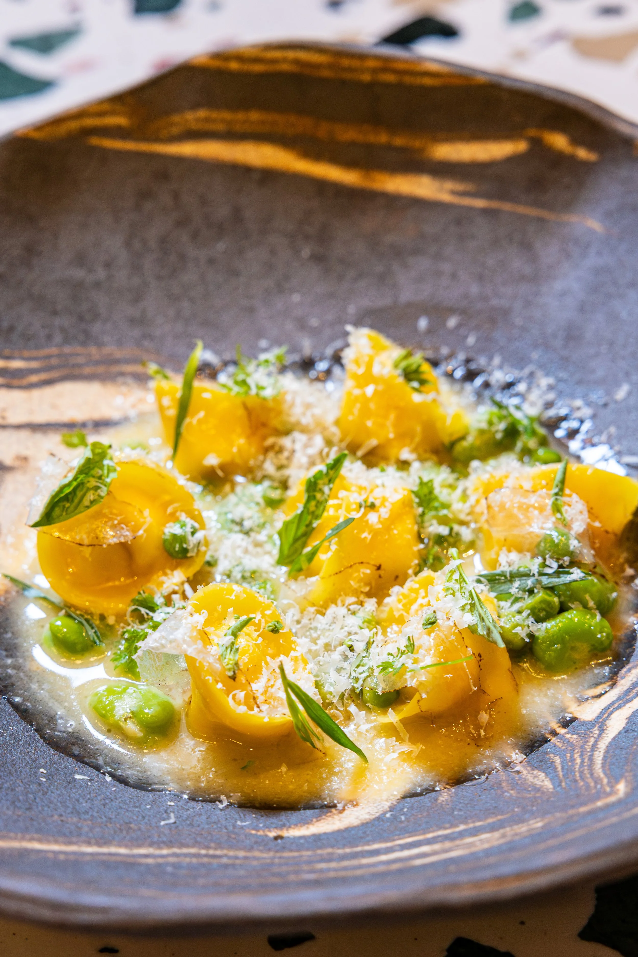 Close-up of a cooked vegetable dish with yellow squash, green peas, and grated cheese served in a black skillet.