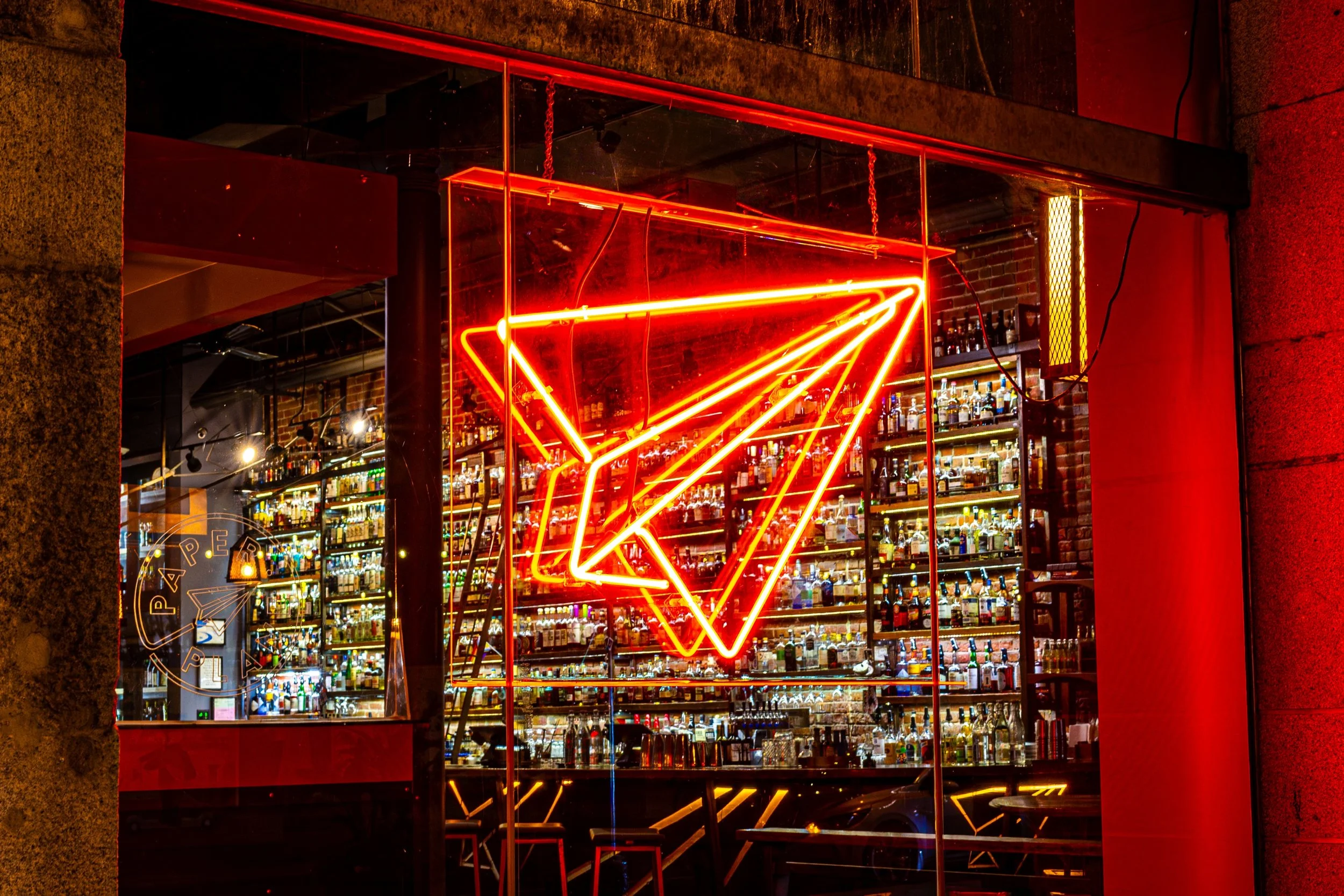 Neon sign of a martini glass outside a bar, with shelves of bottles visible through large glass windows.
