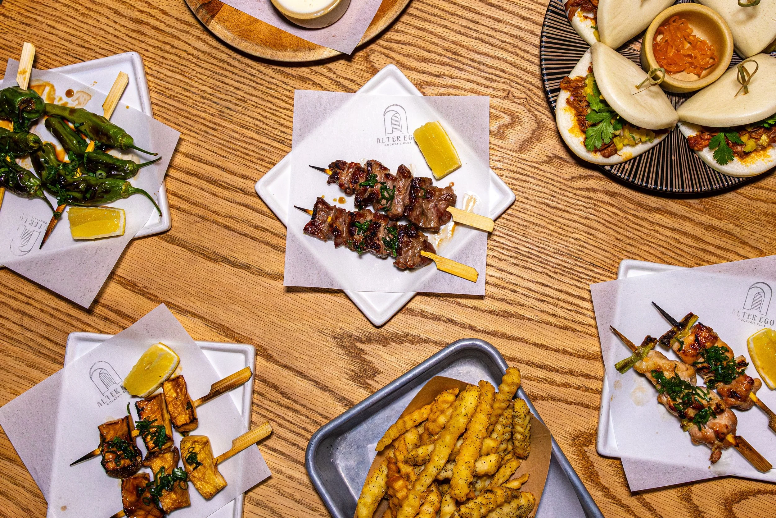 Various Mexican dishes on a wooden table, including grilled skewers, tacos, and fried potato fries.