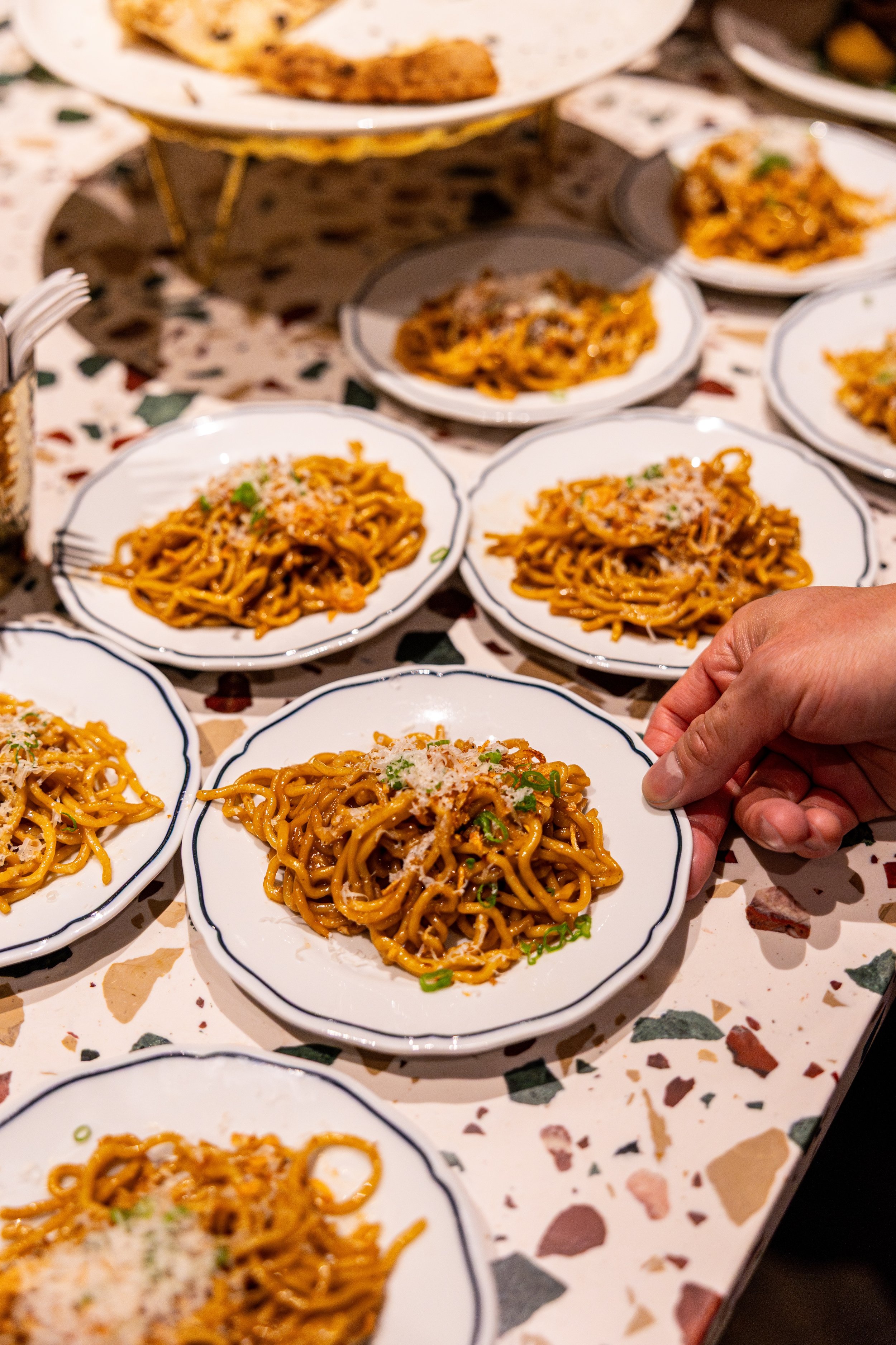 Several plates of cooked noodles garnished with chopped green onions and grated cheese, arranged on a decorative tablecloth.