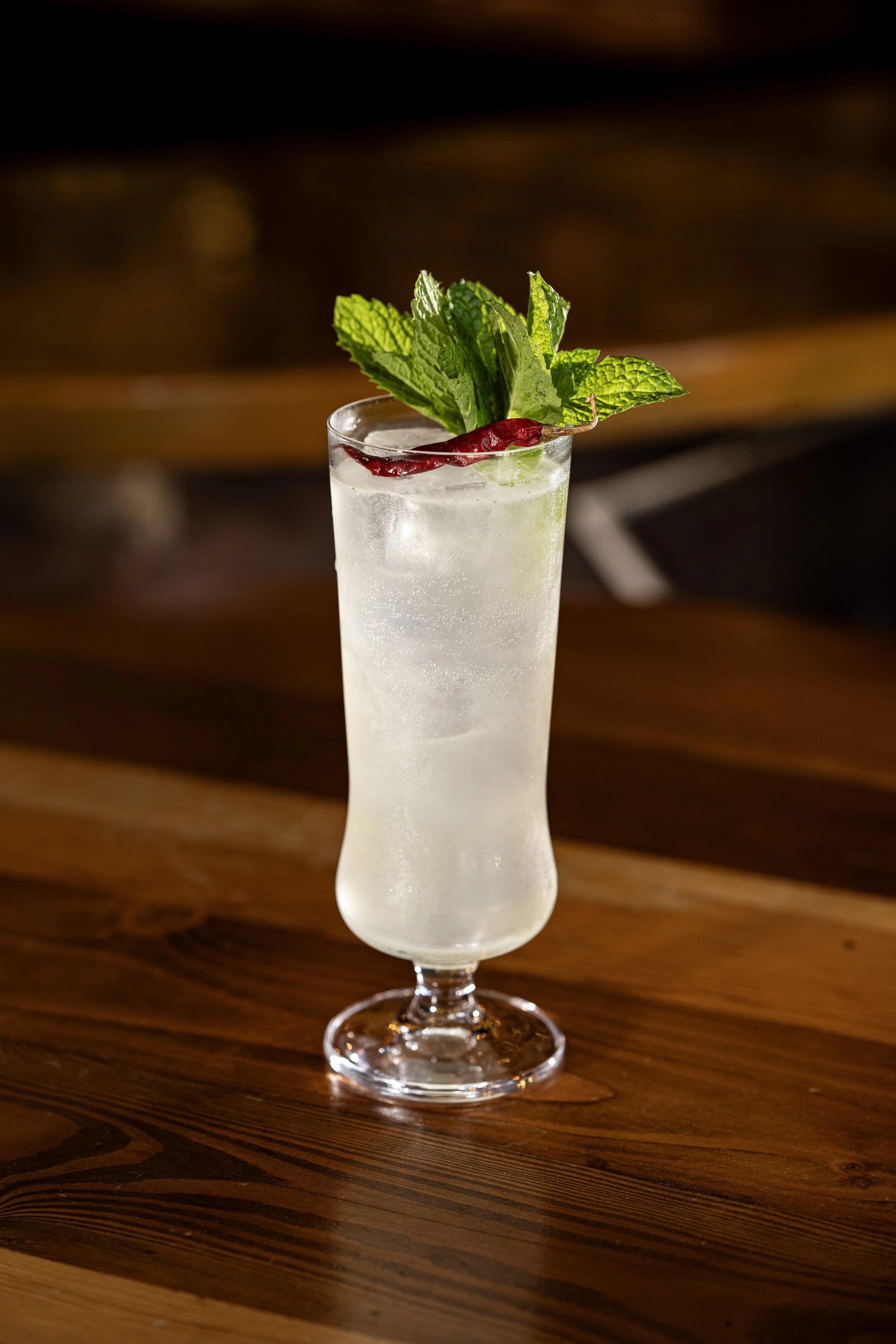 Tall glass of a clear cocktail garnished with mint leaves and a red chili