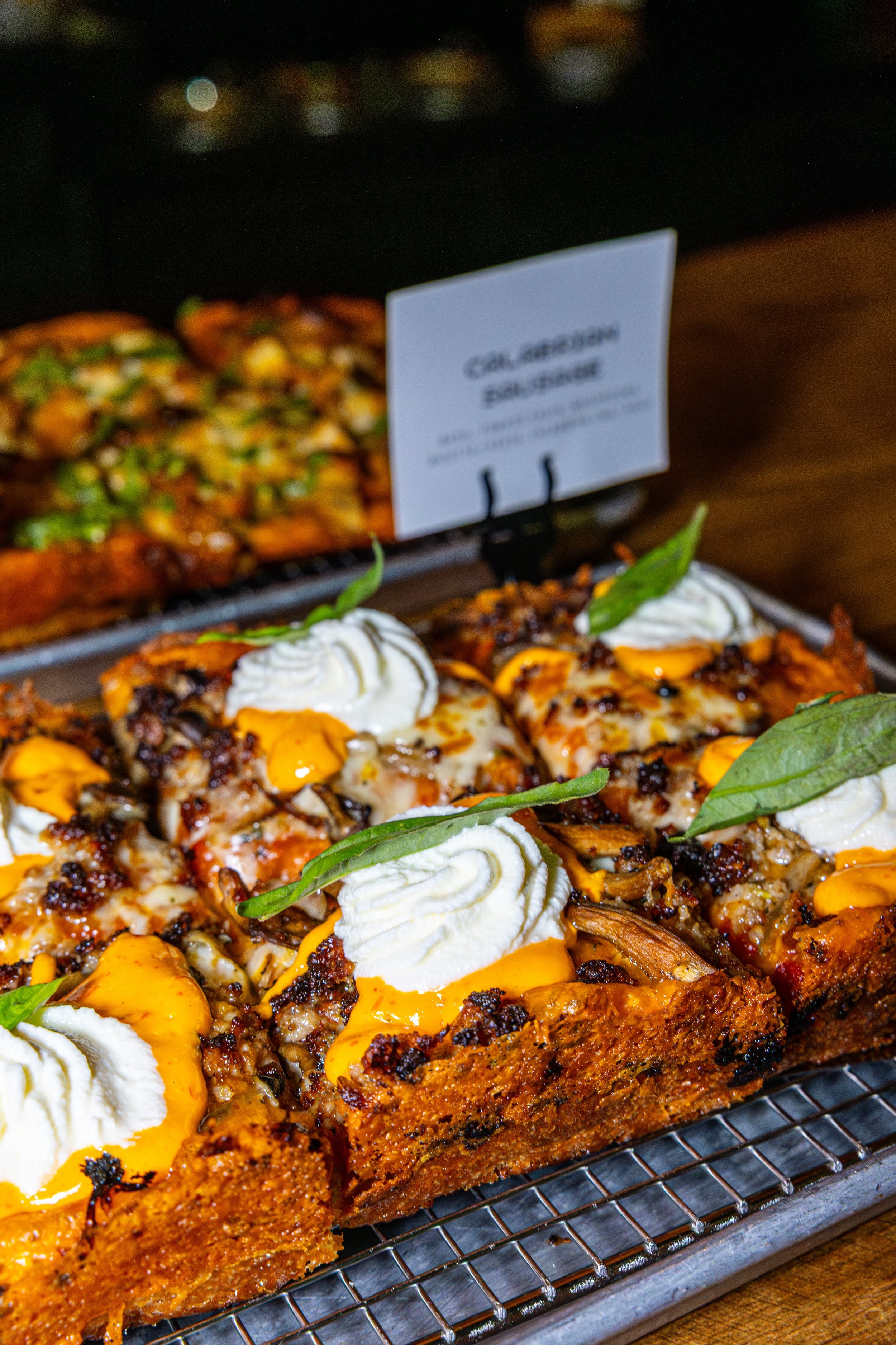 Close-up of a tray of loaded nachos topped with cheese, sour cream, green leaves, and black beans.