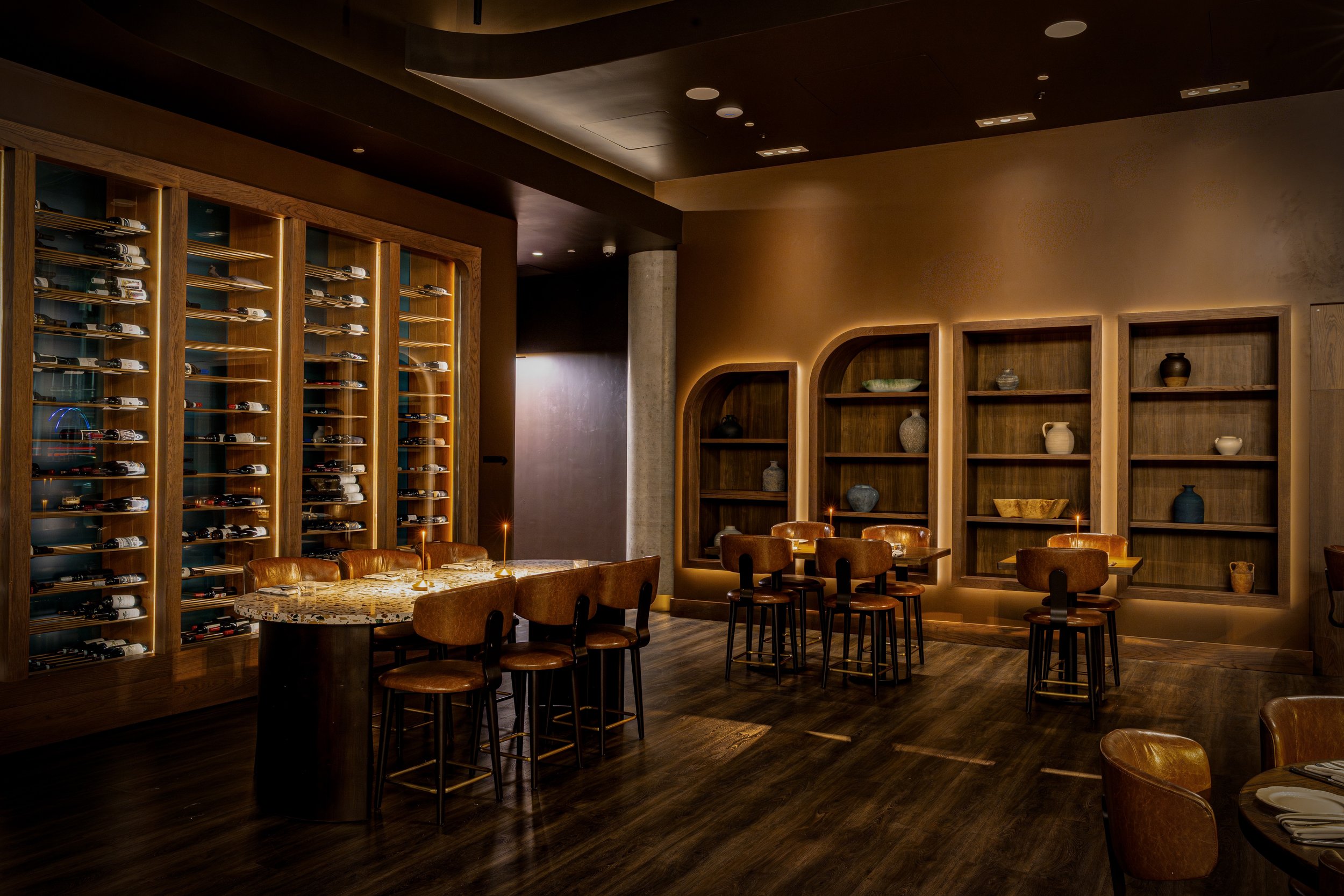 Interior of a upscale restaurant with wooden shelves, decorative pottery, and tables set for dining with candles.