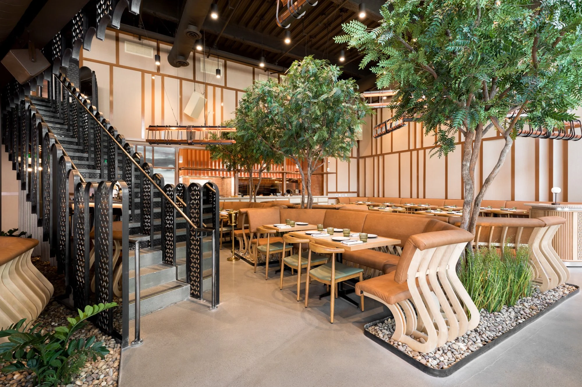 Interior of a modern restaurant with large indoor trees, wooden furniture, and decorative lighting.