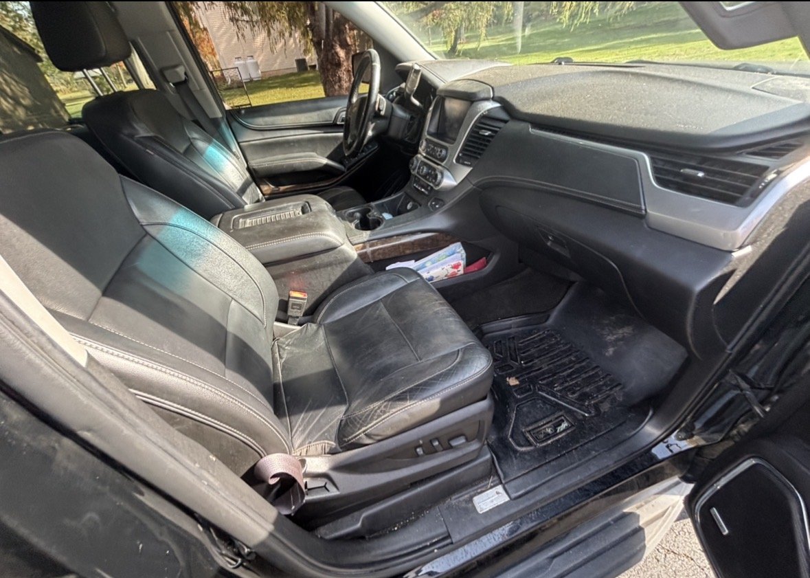 Interior of a black vehicle showing the front seats, dashboard, and center console, with sunlight reflecting off the leather seats.