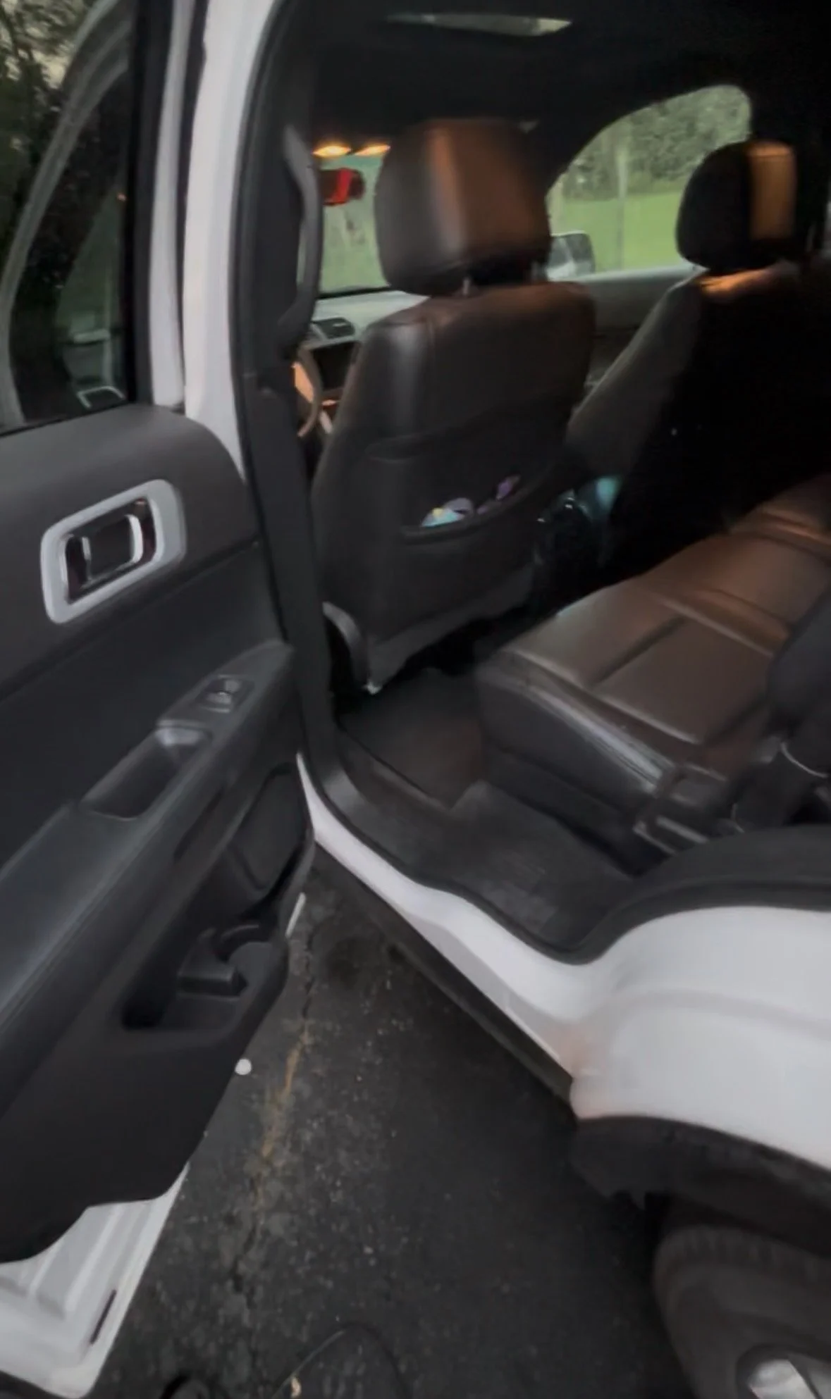 The interior of a black and white SUV showing the back seat area with black leather seats, a backs of the front seats, and the open rear passenger door with window control panel.
