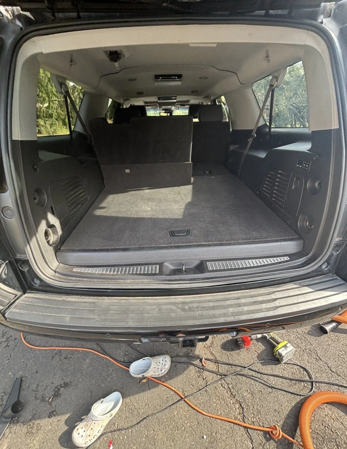 Open trunk of a black SUV showing the spacious cargo area with rear seats folded down, surrounded by tools and electrical cords on the ground.