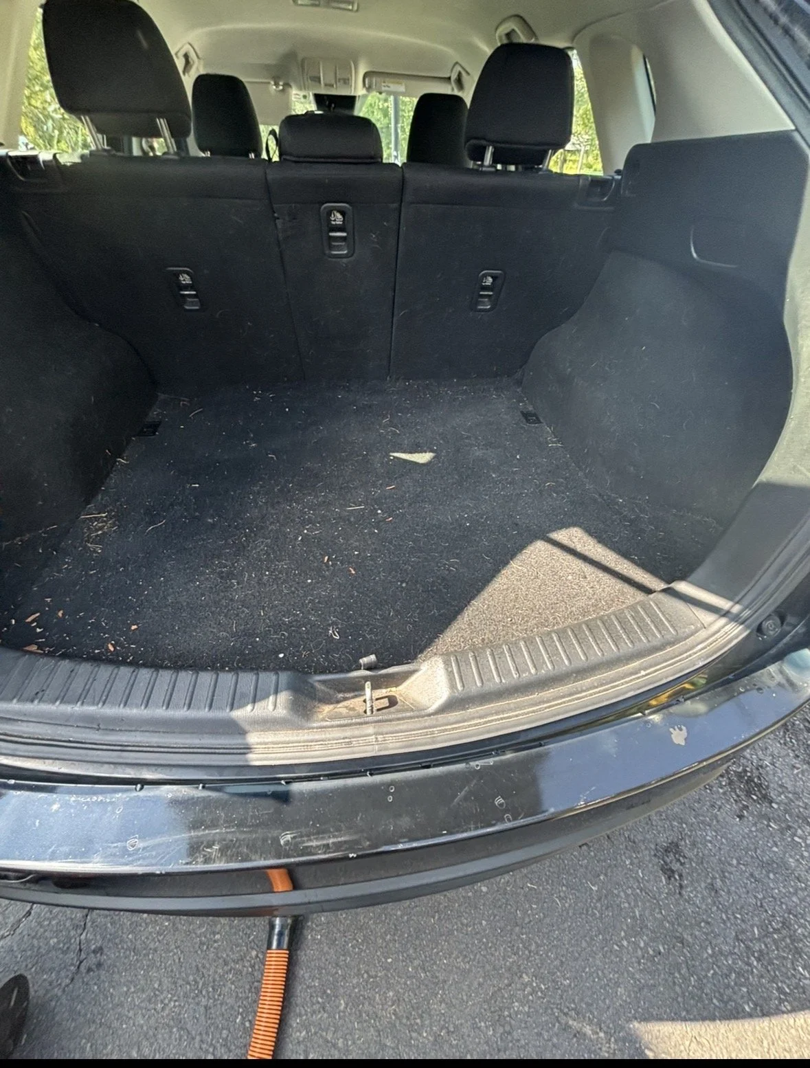 The open trunk of a black SUV with a black interior, showing the cargo space with some dirt and debris, and part of the battery disconnect cable at the bottom.
