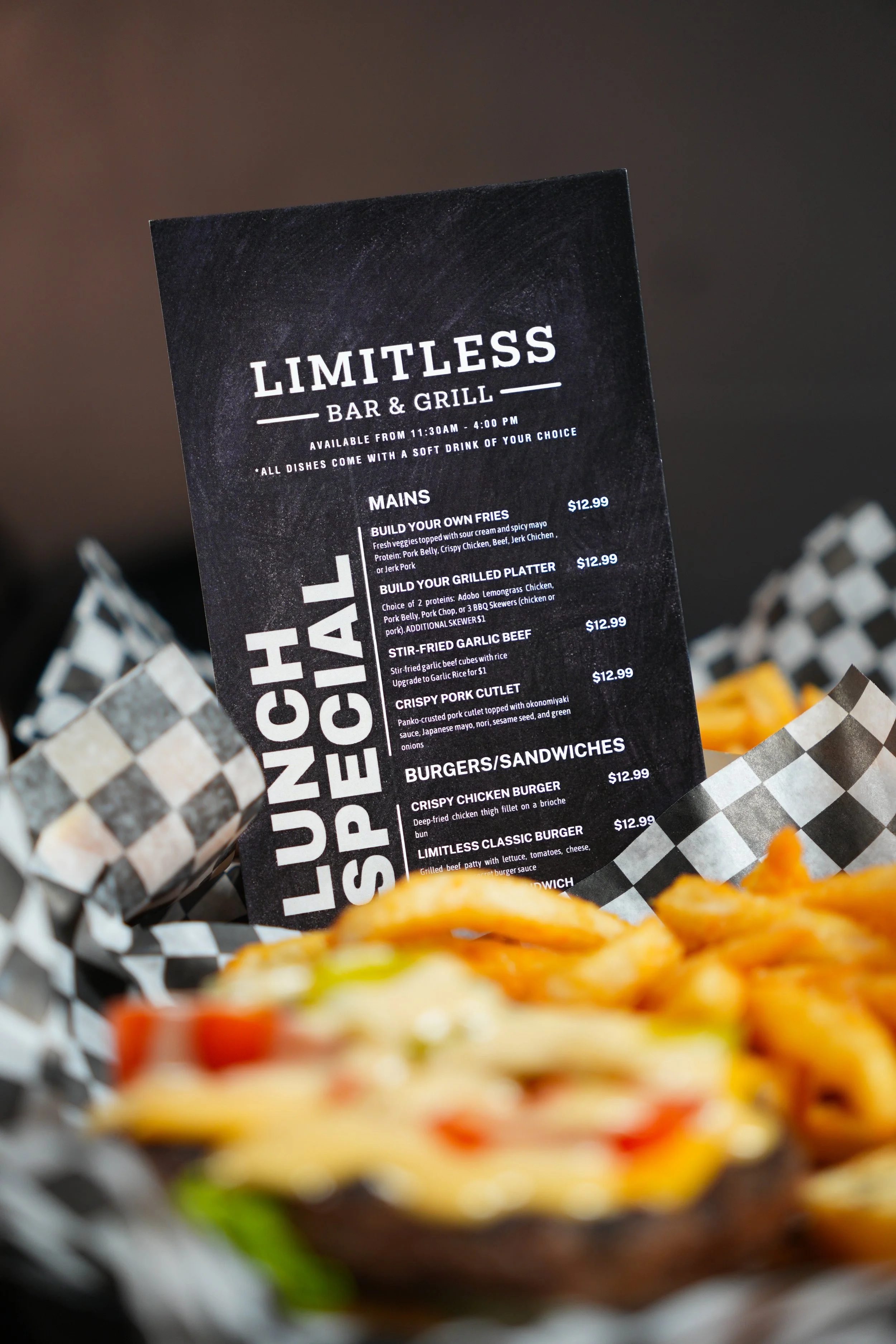 A black menu board titled 'LIMITLESS BAR & GRILL' with food options listed, placed among baskets of food with checkered paper lining.