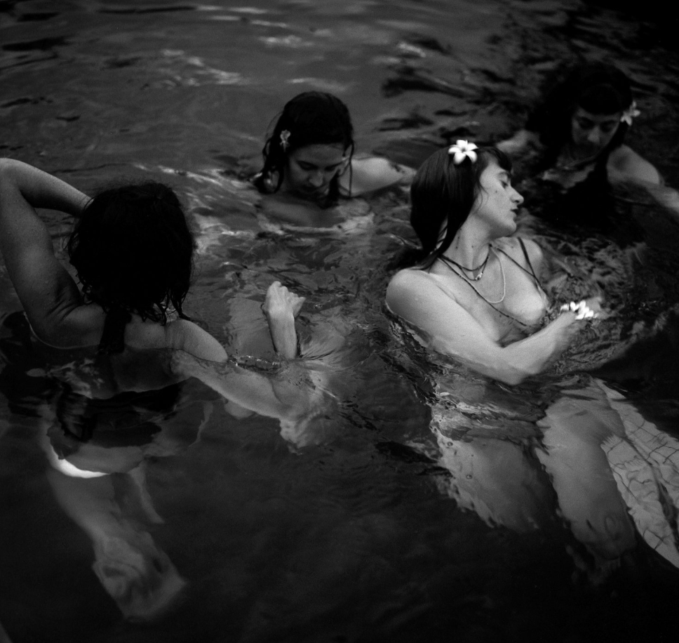 Four women swimming in the water, some with flowers in their hair, appearing relaxed and enjoying themselves.