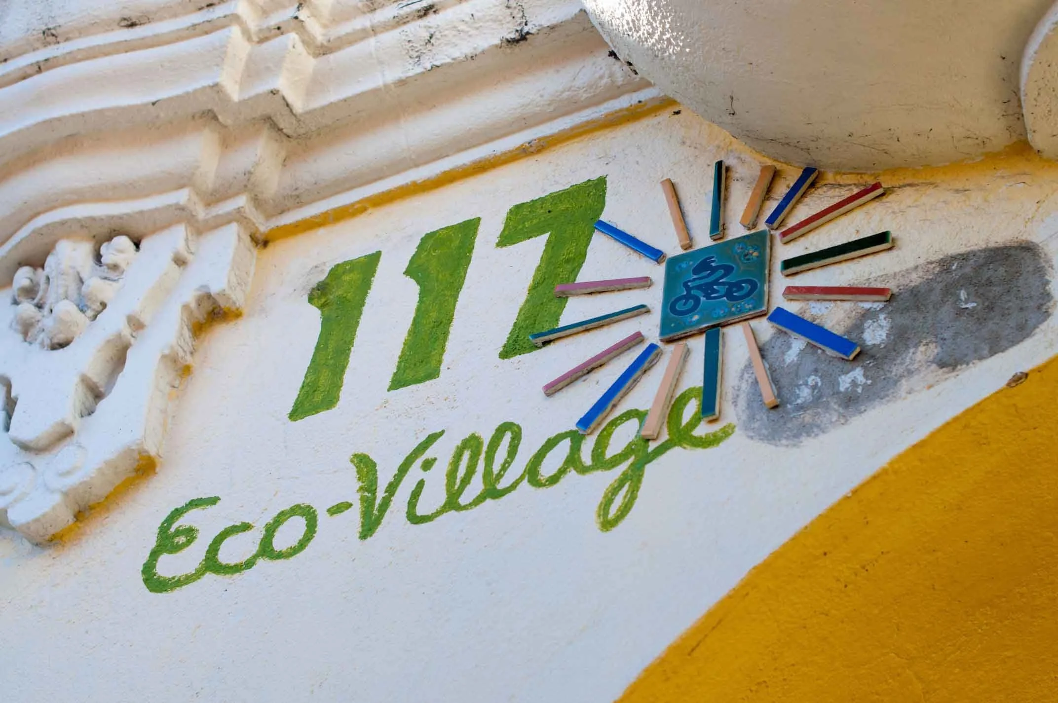 Close-up of a yellow and white wall with a colorful chalk clock showing a time of 11:00 and a green hand-lettered sign that reads 'Eco-friendly'.