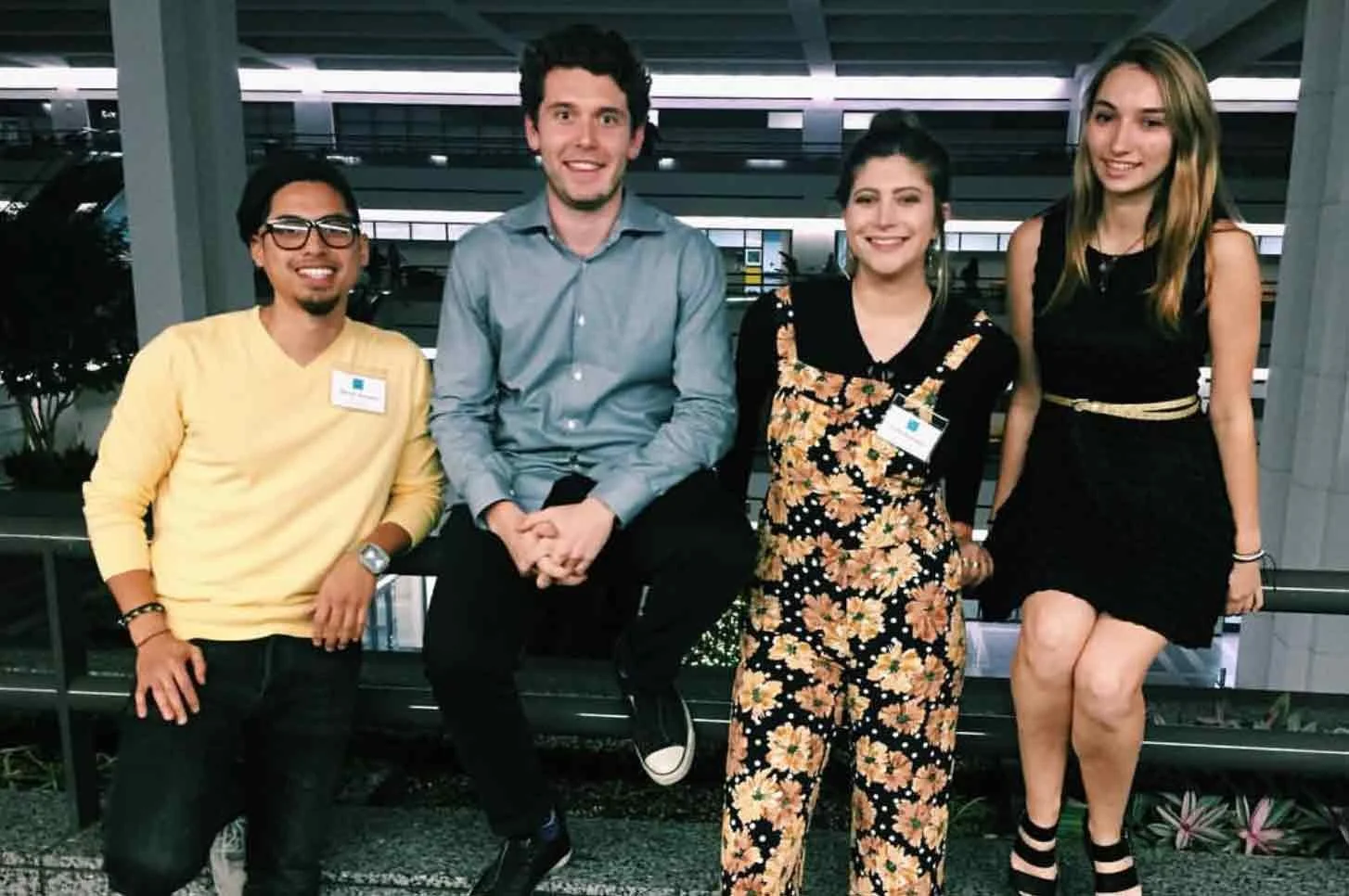 Group of four young adults posing and smiling at a semi-outdoor setting in the evening.