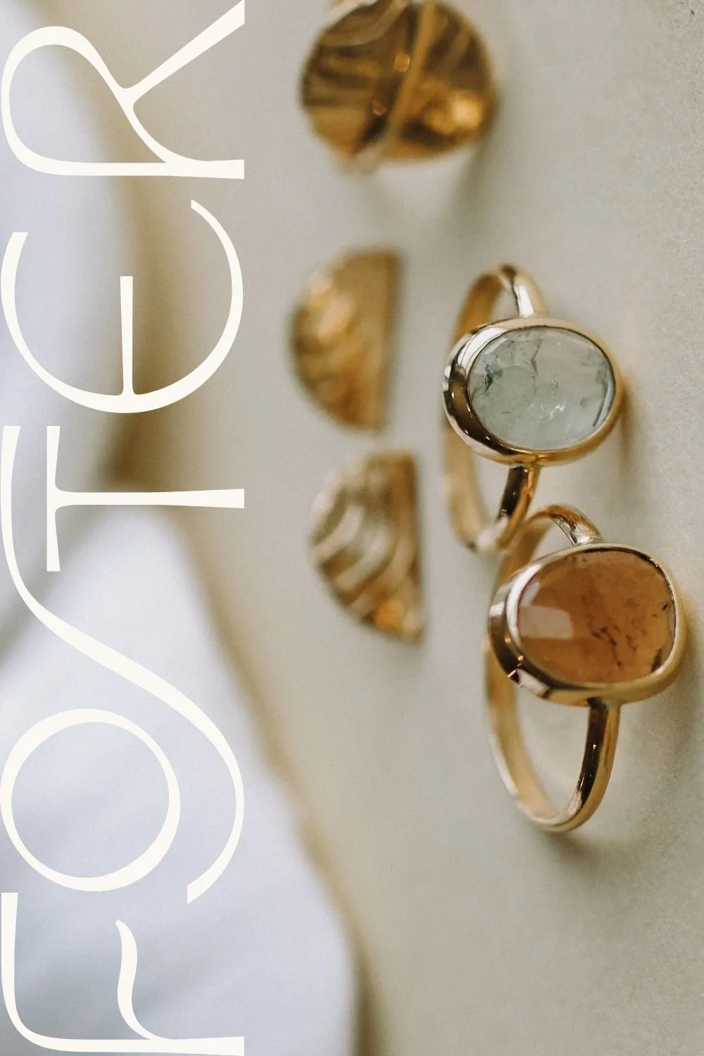 Close-up of two gold rings with semi-precious stones, one with a clear stone and the other with an orange-brown stone, lying on a light surface.