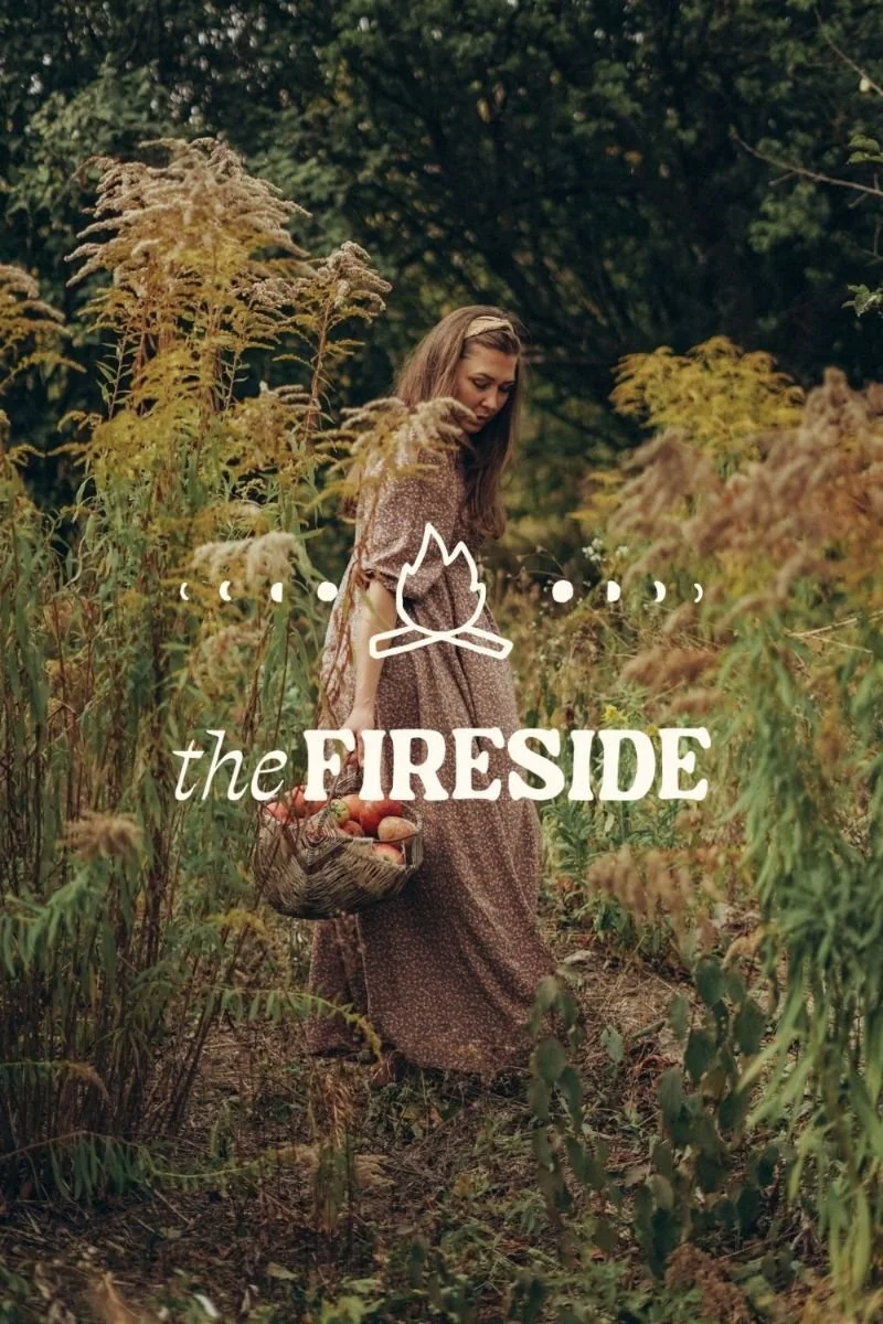 A woman in a brown patterned dress walking through a field of tall grasses and wildflowers, holding a basket of apples, with trees in the background, overlaid with a camping fire icon and the text "the FIRESIDE".