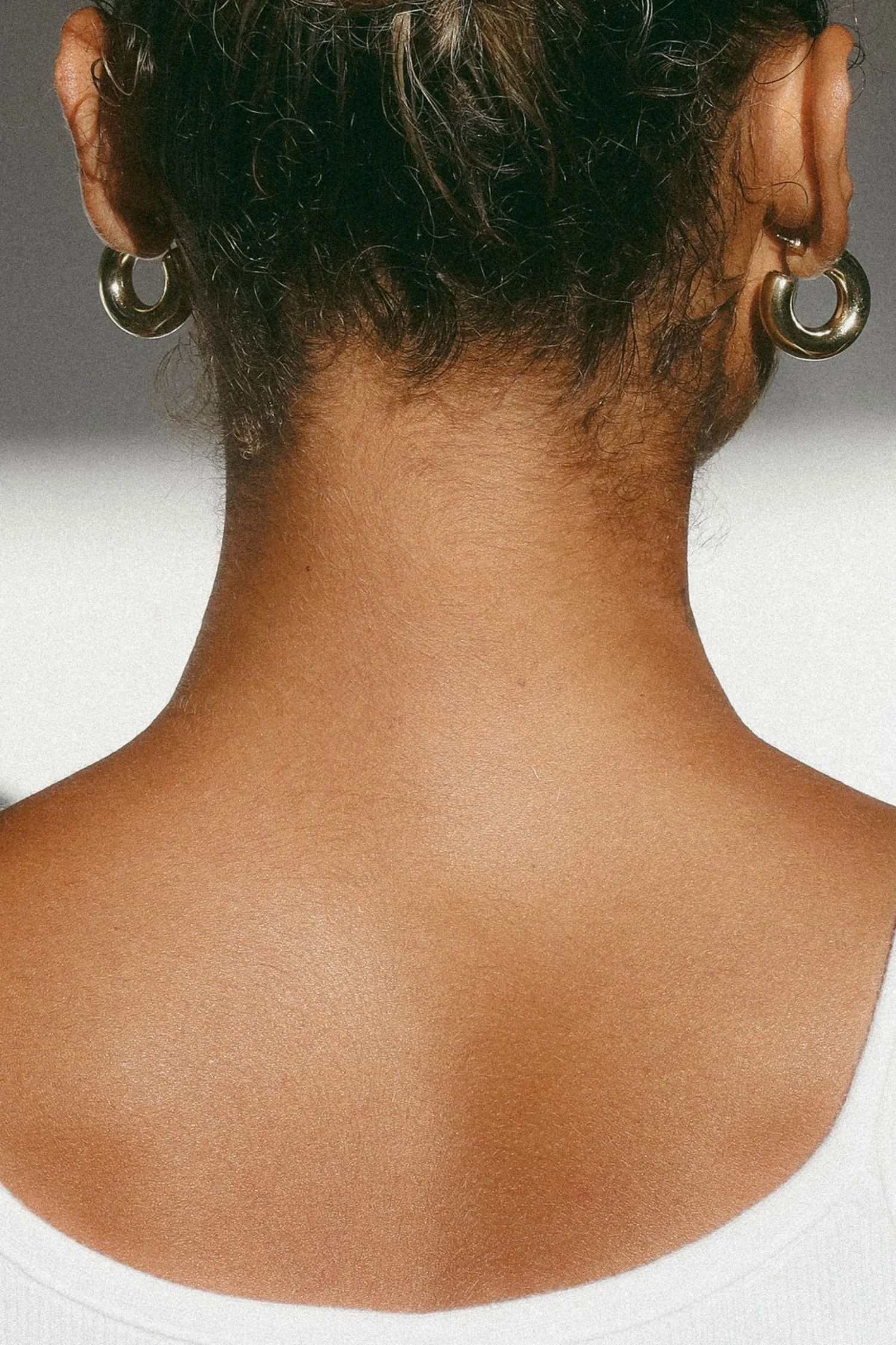 Back of a person's neck and upper back, with short, wavy dark hair and large silver hoop earrings.