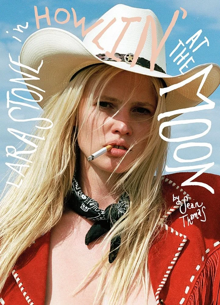 A woman with long blonde hair wearing a white wide-brimmed hat, a black bandana, and a red jacket, holding a cigarette in her mouth. The background is blue, and the image has white text overlay reading "in love with the howlin' at the moon" and "by Jean Torms."