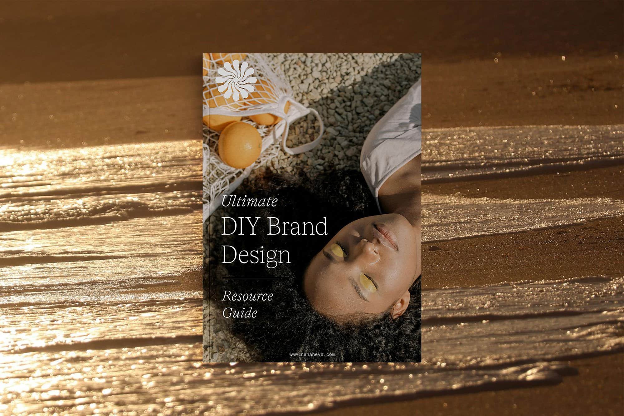 A book titled 'Ultimate DIY Brand Design Resource Guide' lying on a wooden surface with a woman resting her head on the cover, her eyes closed, wearing eye makeup and a white top.