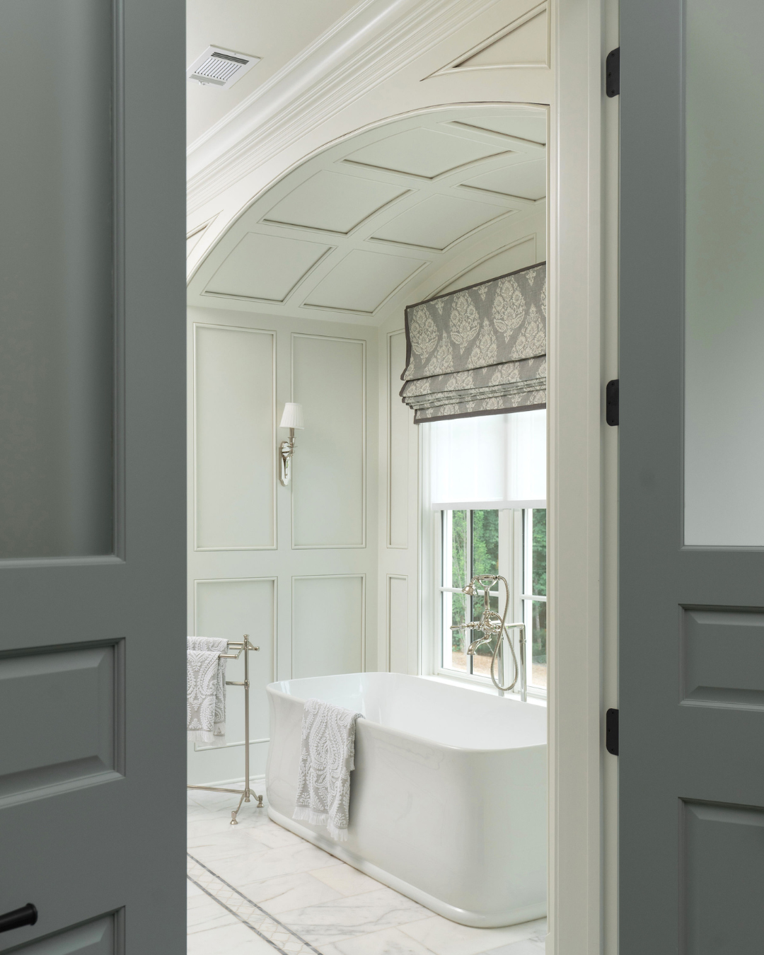 Elegant bathroom with a freestanding bathtub near a window, light-colored paneled walls, and decorative ceiling design.