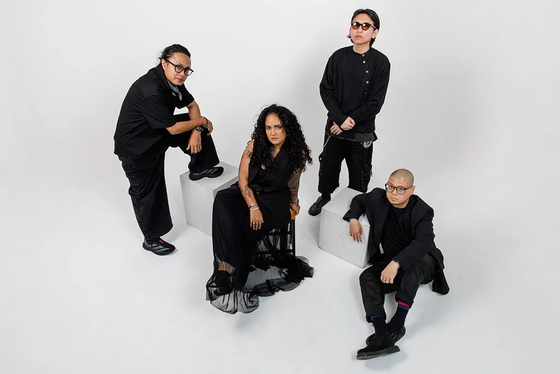 Group of four diverse individuals in black clothing posing against a plain white background.
