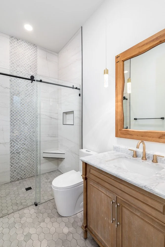 Modern bathroom with walk-in shower, toilet, and wooden vanity with marble countertop and mirror.