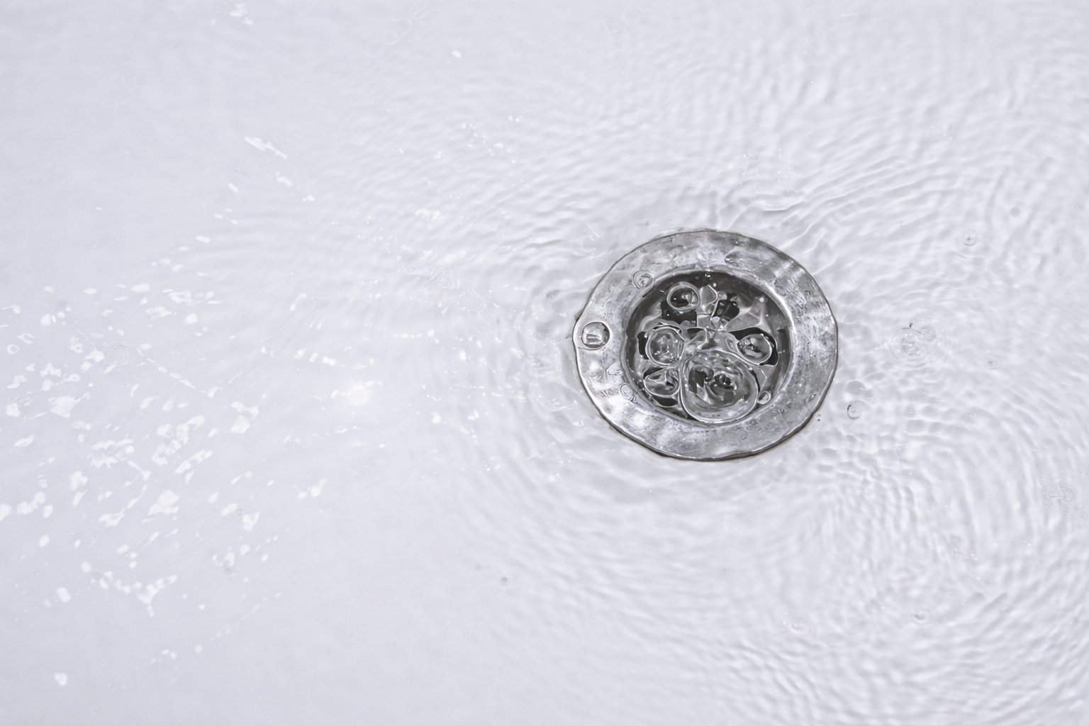 Close-up of a metal sink drain with bubbles and water swirling around it