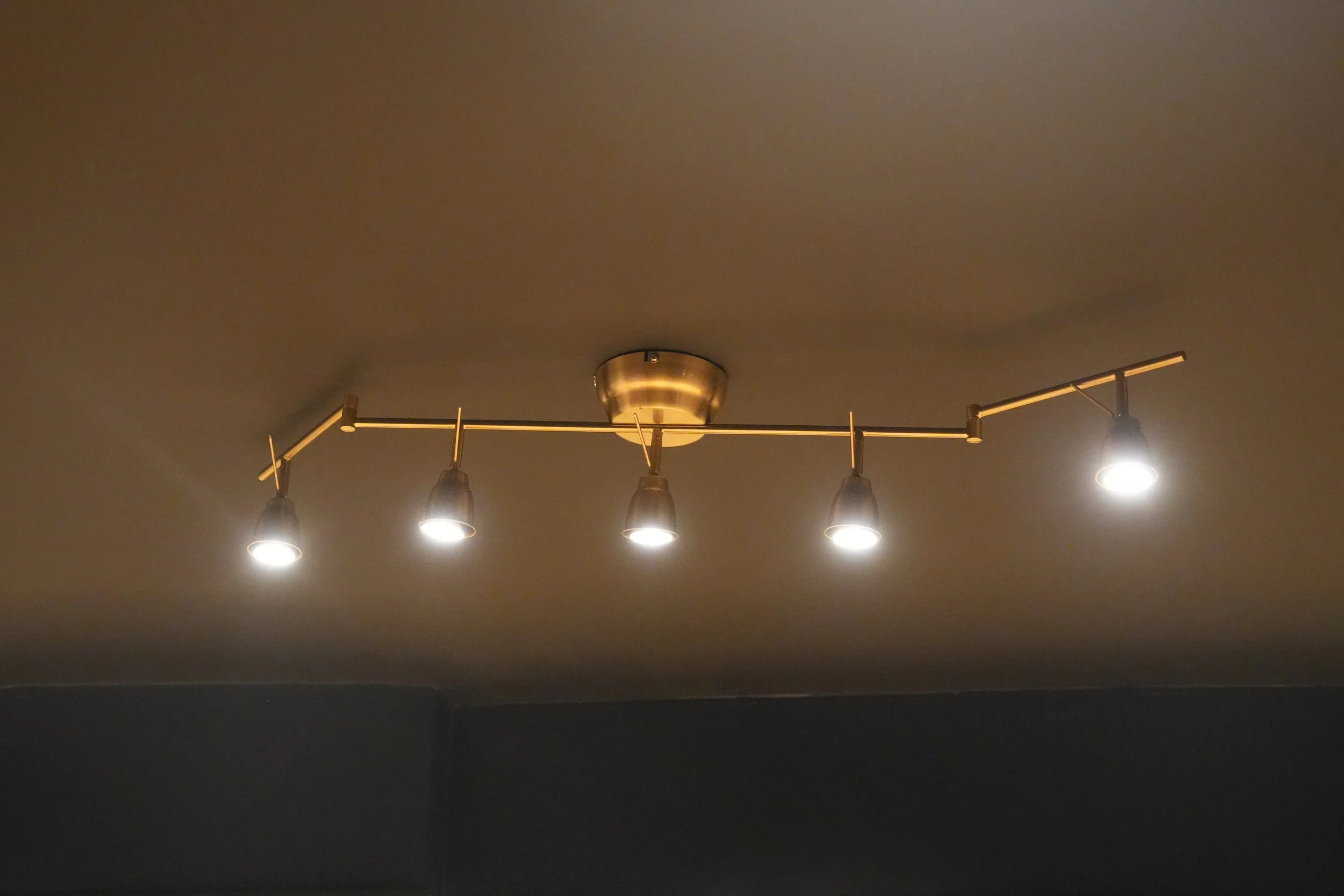 Ceiling light fixture with four adjustable spotlights mounted on a horizontal bar with a round mount.