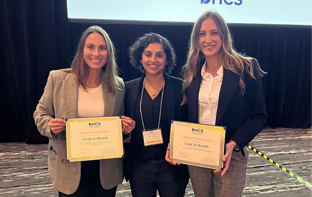 Three women standing together inside a conference room, holding certificates of recognition, smiling at the camera.