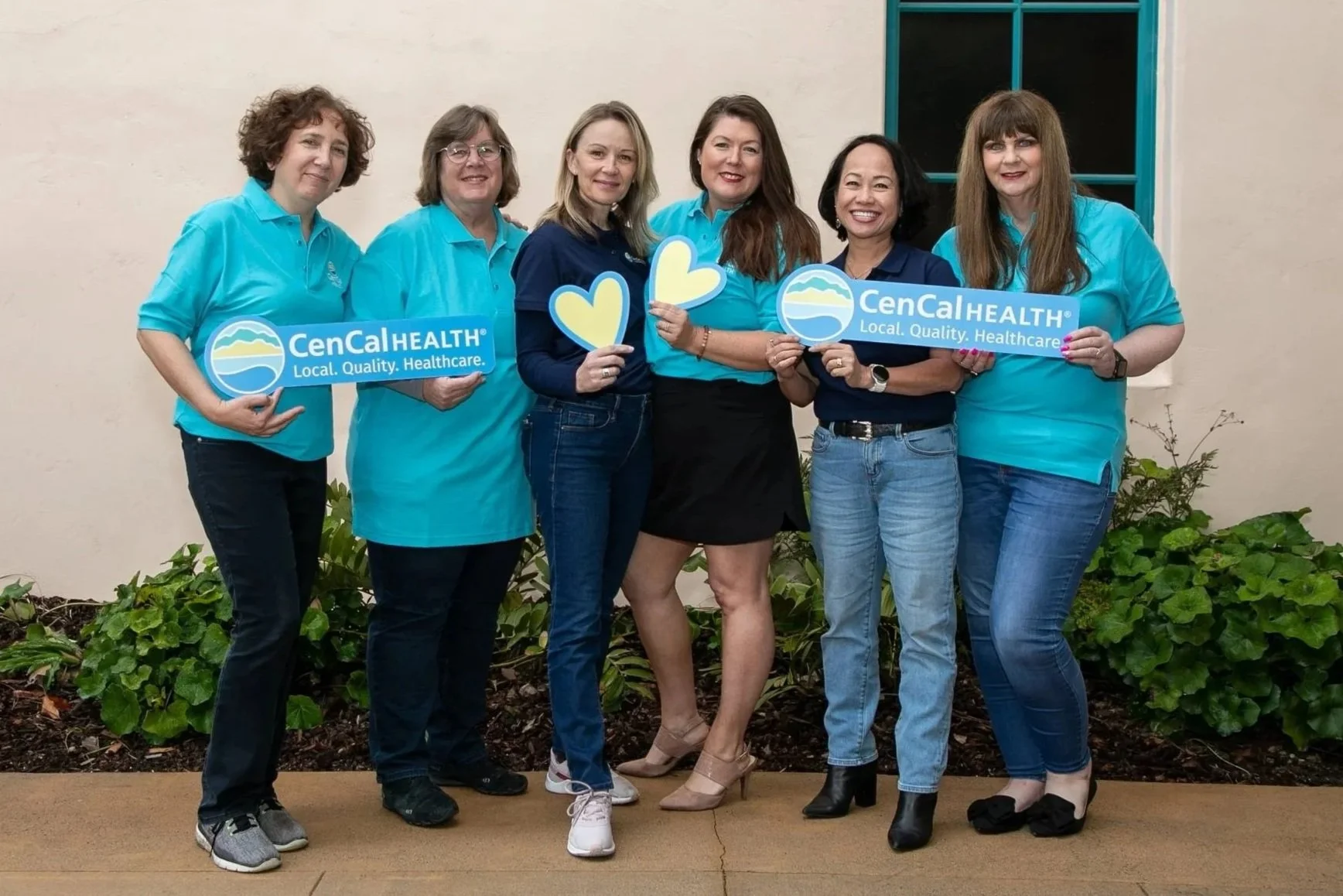 Group of six women standing outdoors, holding signs that say 'CenCalHEALTH' and 'Local. Quality. Healthcare.', smiling at the camera.