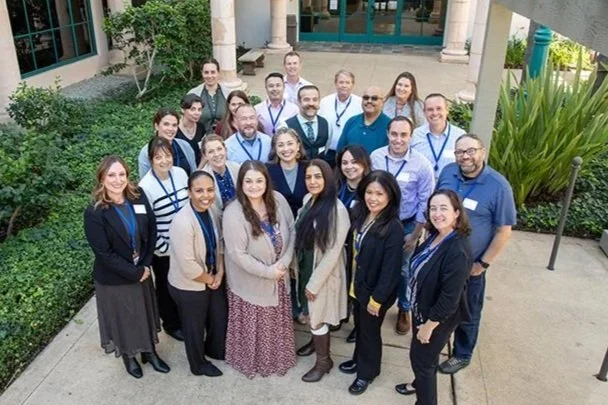 Group of 20 diverse professionals standing outdoors, smiling and posing for a group photo.