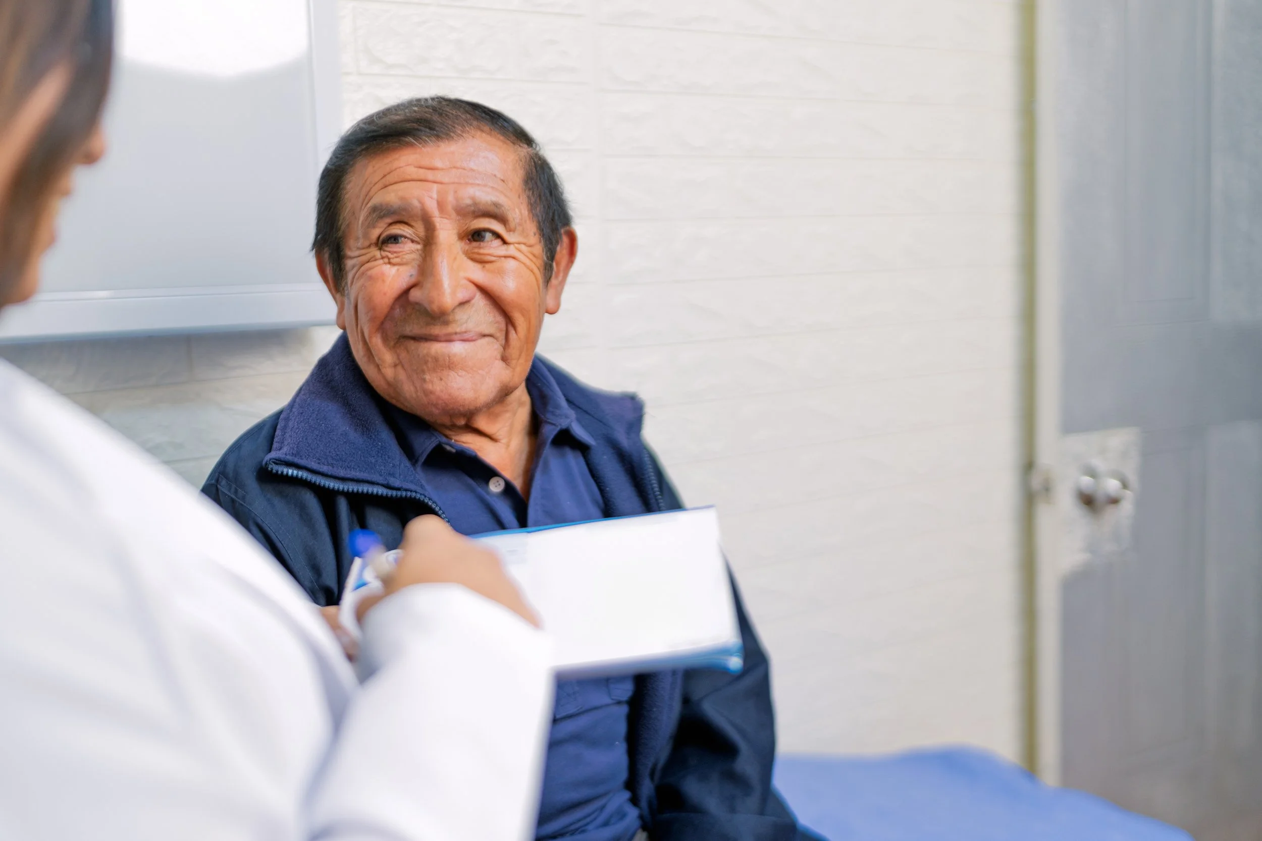 An elderly man smiling while talking to a healthcare professional in what appears to be a medical facility.