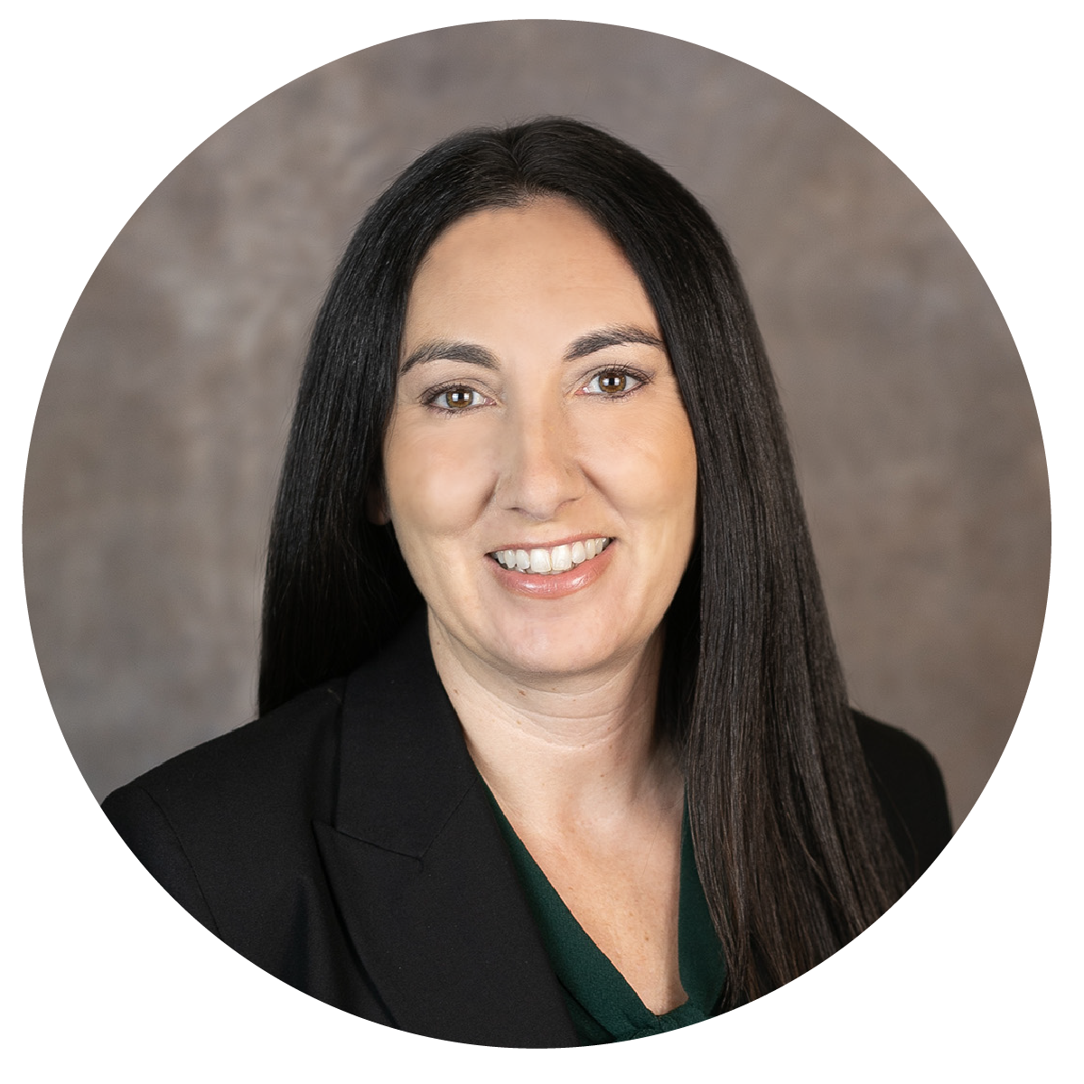 A woman with long dark hair smiling, wearing a black blazer and dark green top, in front of a neutral gray background.