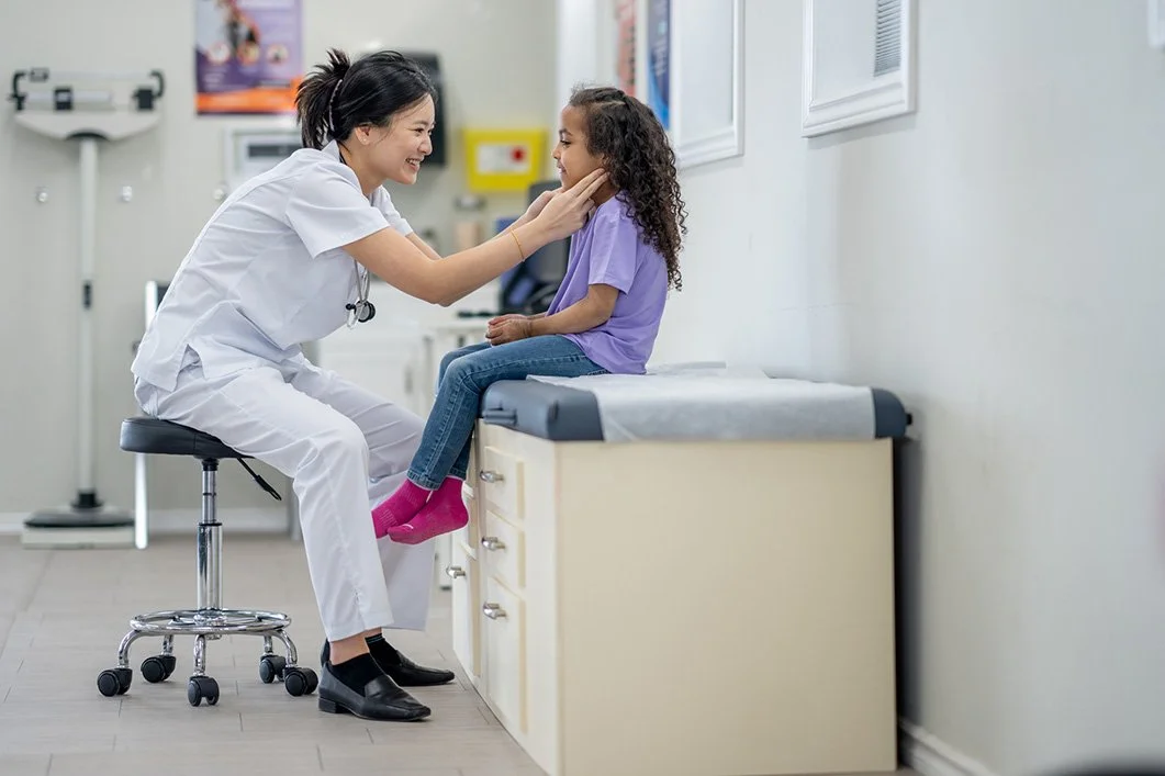 A female doctor gently holds a young girl's chin and looks at her with a smile in a doctor's office.