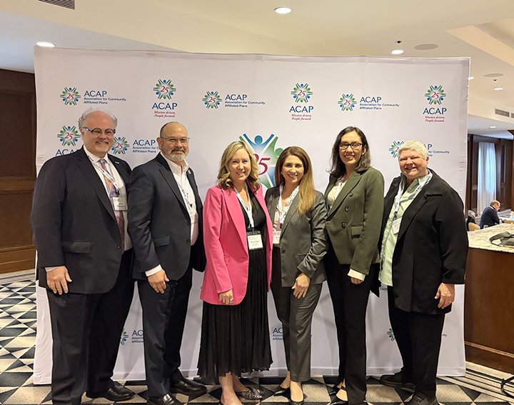 Group of six professionals standing in front of a step and repeat banner with the ACAP logo at a conference.