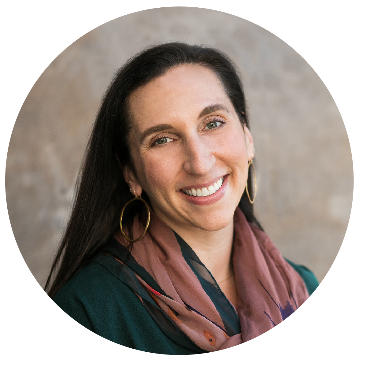 Close-up portrait of a smiling woman with long dark hair, wearing gold hoop earrings and a multicolored scarf, against a neutral background.
