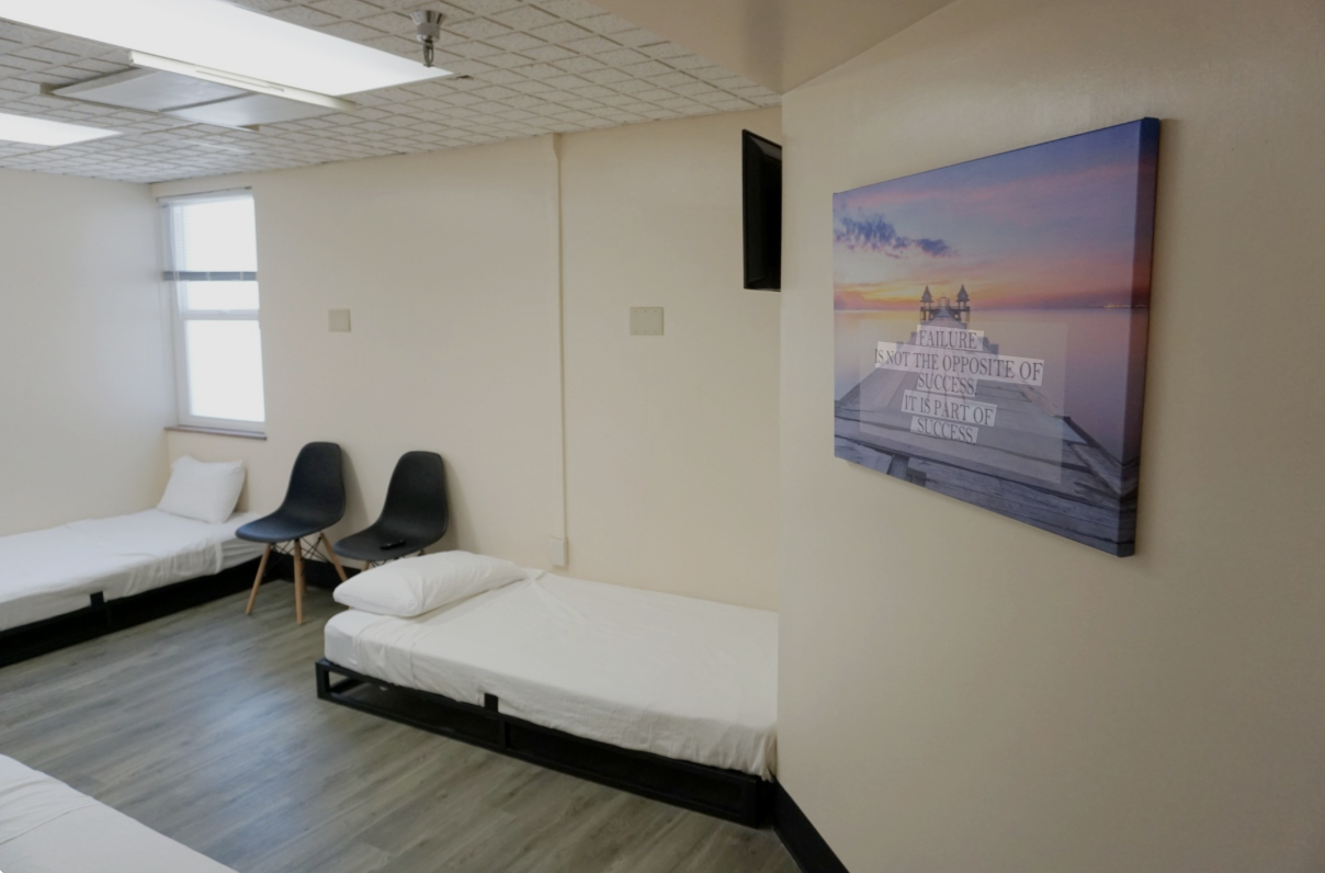 A room with three beds, two black chairs, a window, and a wall with a sunset picture with an inspirational quote. The quote says, 'Failure is not the opposite of success. It is part of success.'