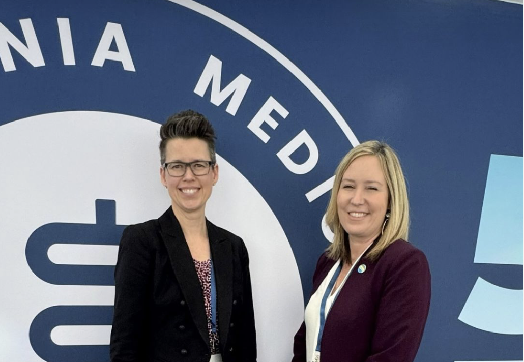 Two women standing in front of a Pennsylvania Medical logo wall, smiling at the camera.