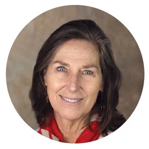 A close-up portrait of an older woman with dark hair, smiling, wearing a red and white scarf, against a neutral background.