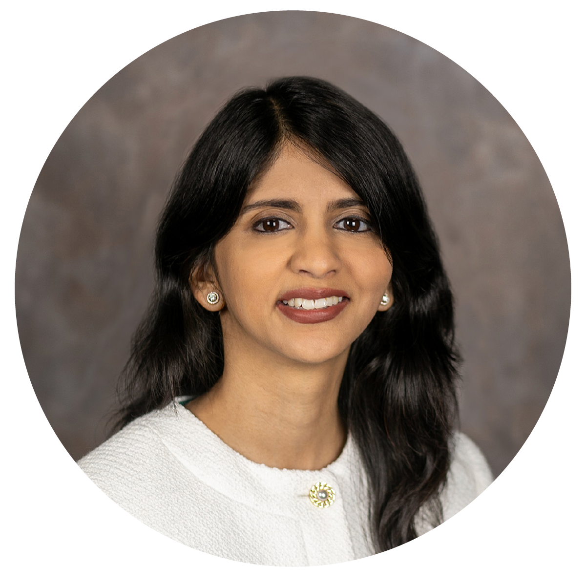 A professional woman with long dark hair, wearing a white textured top, pearl earrings, and a brooch, smiling softly against a neutral background.