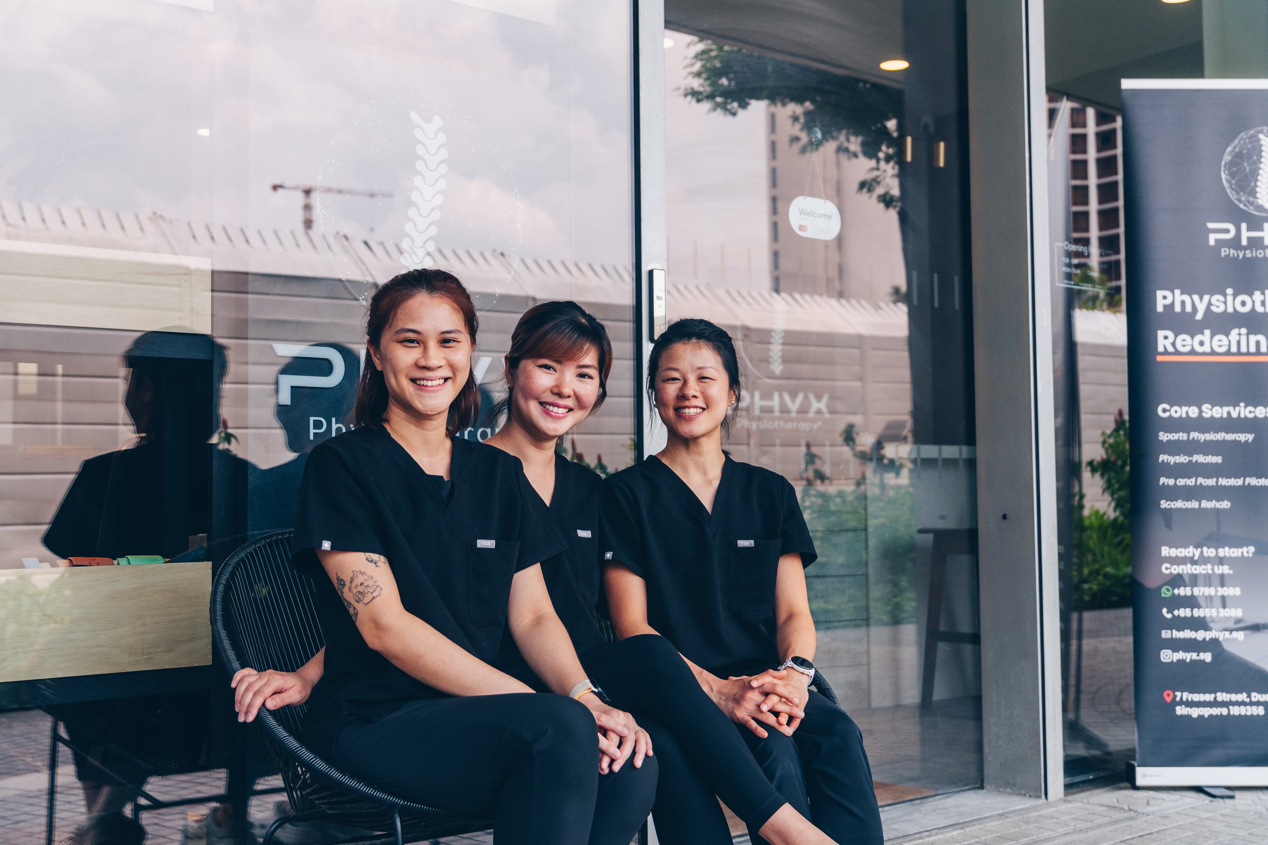 Three smiling female physiotherapists sitting outside a clinic.