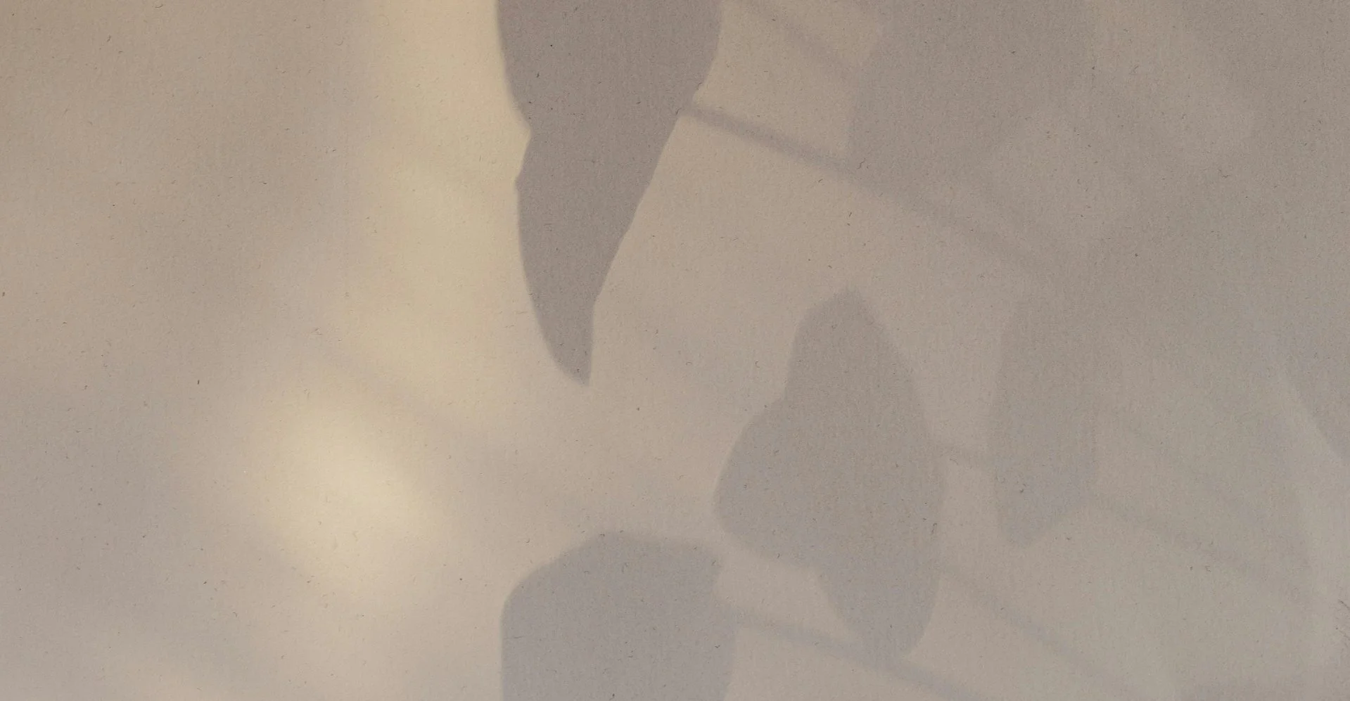 Silhouette of a person lying on their side on a bed or surface with a light-colored wall in the background.