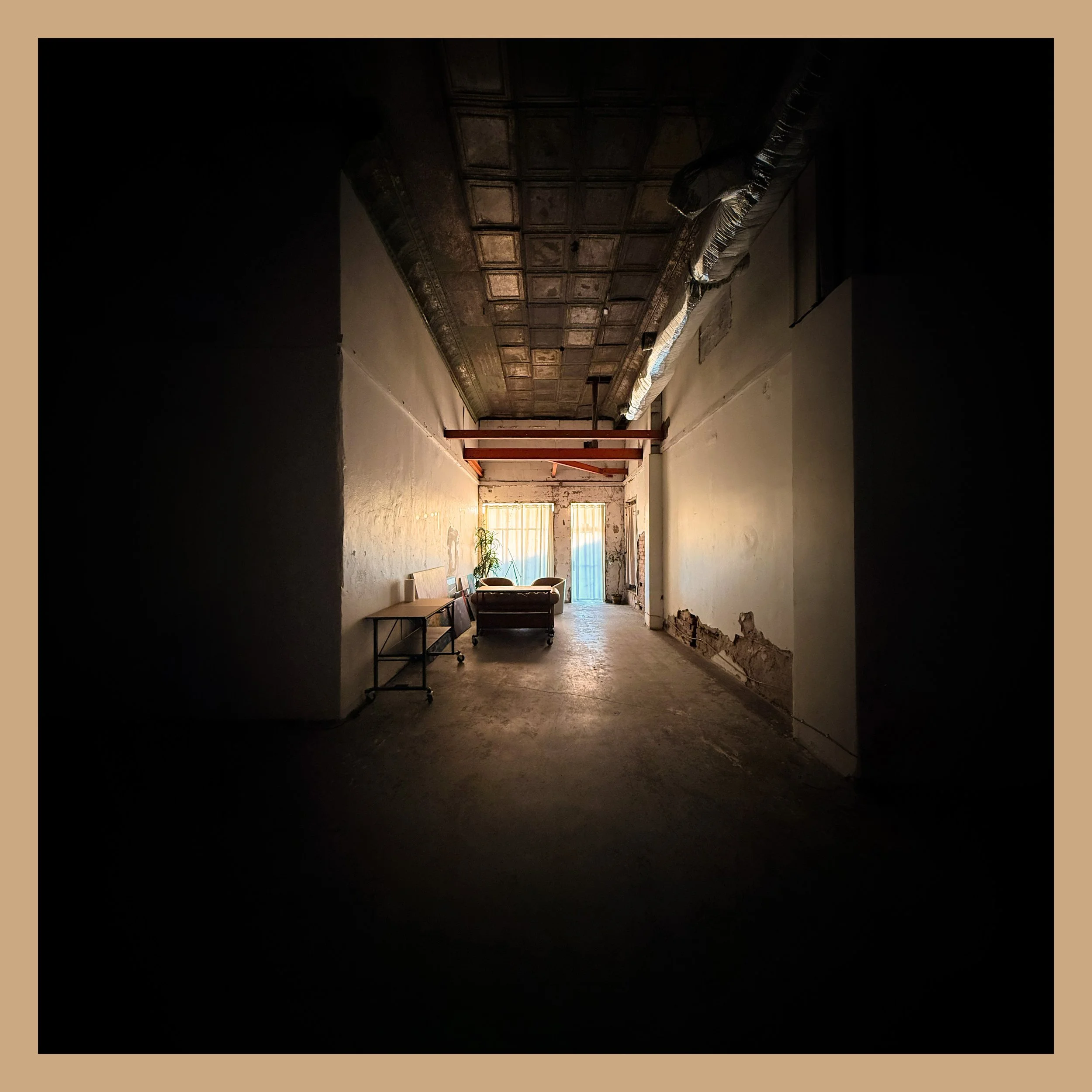 A dimly lit hallway with an ornate ceiling, exposed ductwork, and some furniture including a couch and tables at the end of the hallway.