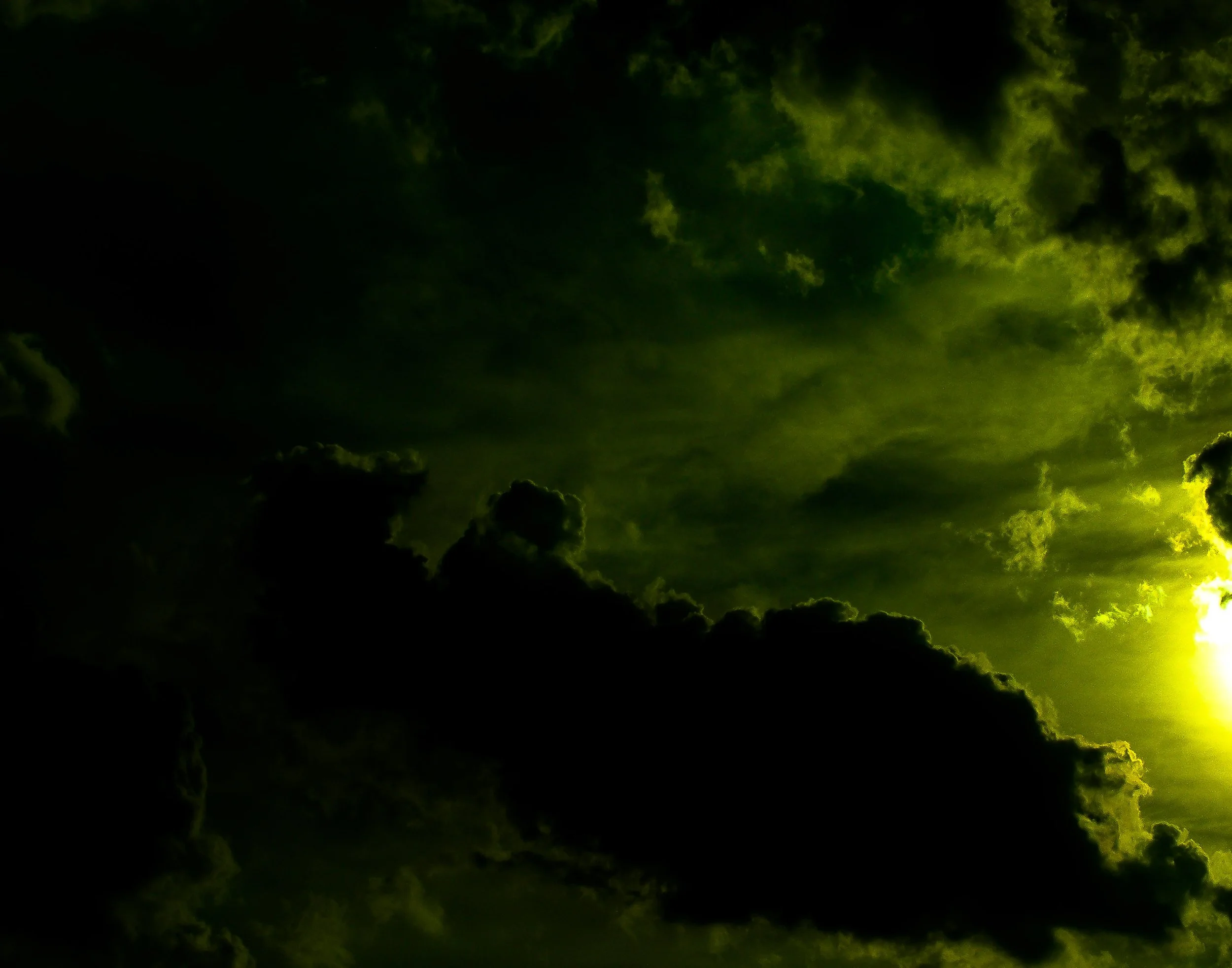 Dark cloudy sky with the sun partially visible on the right side, casting a yellowish-green glow through the clouds.