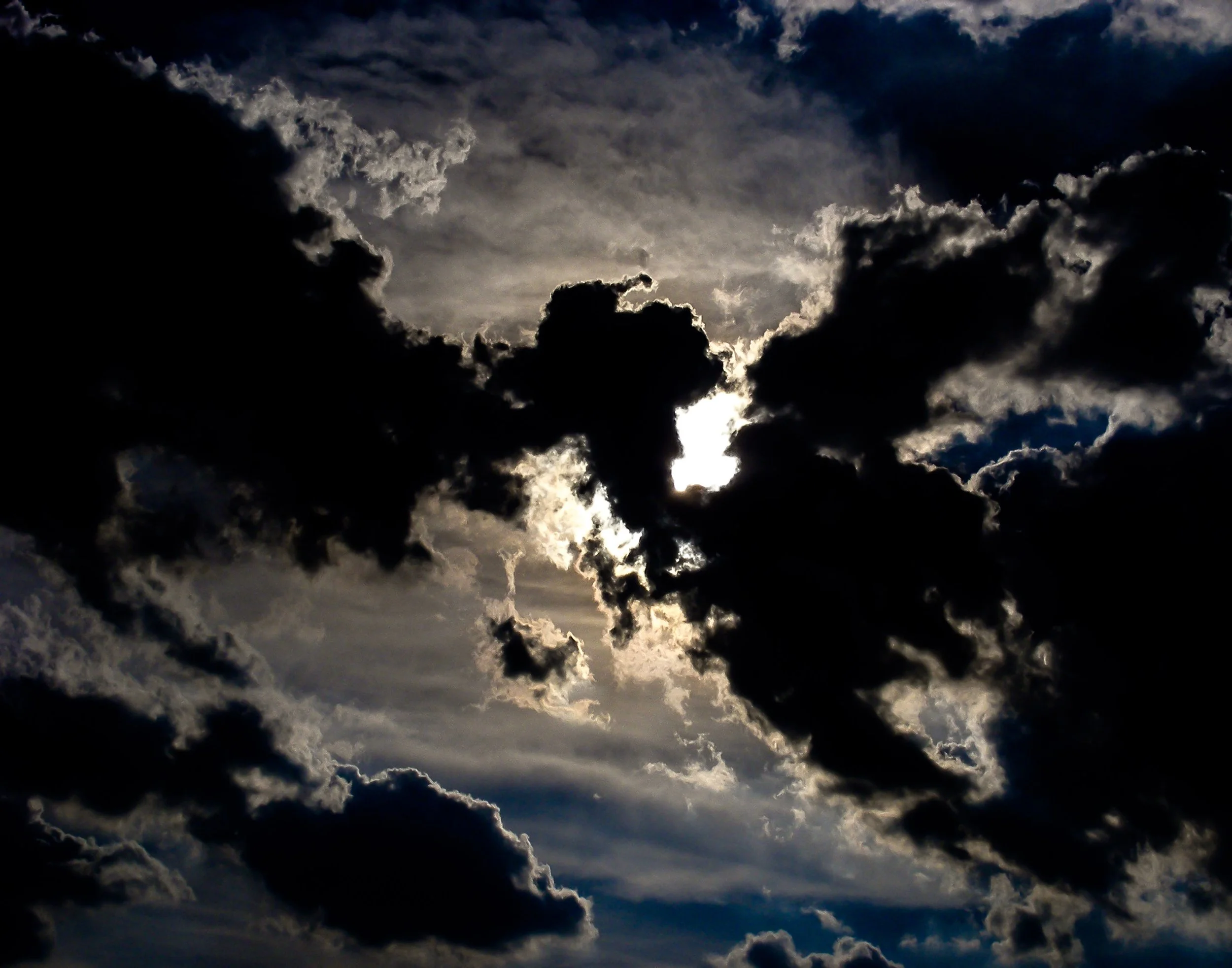 Dark clouds partially covering the sun in a cloudy sky.
