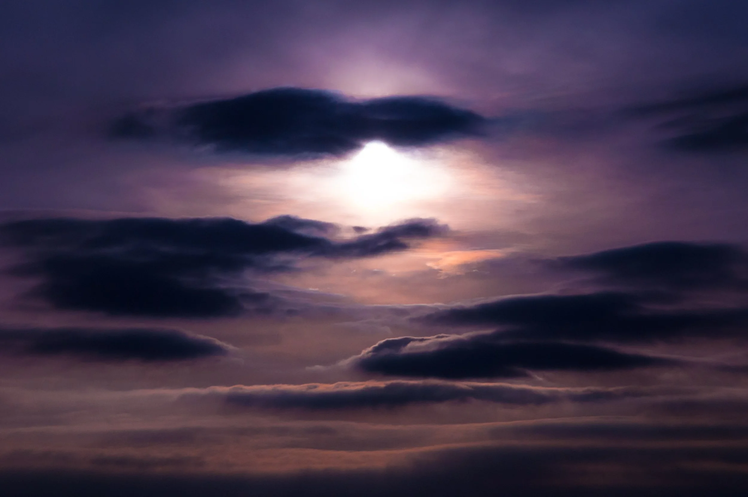 Moon partially obscured by dark clouds against a purple and pink sky