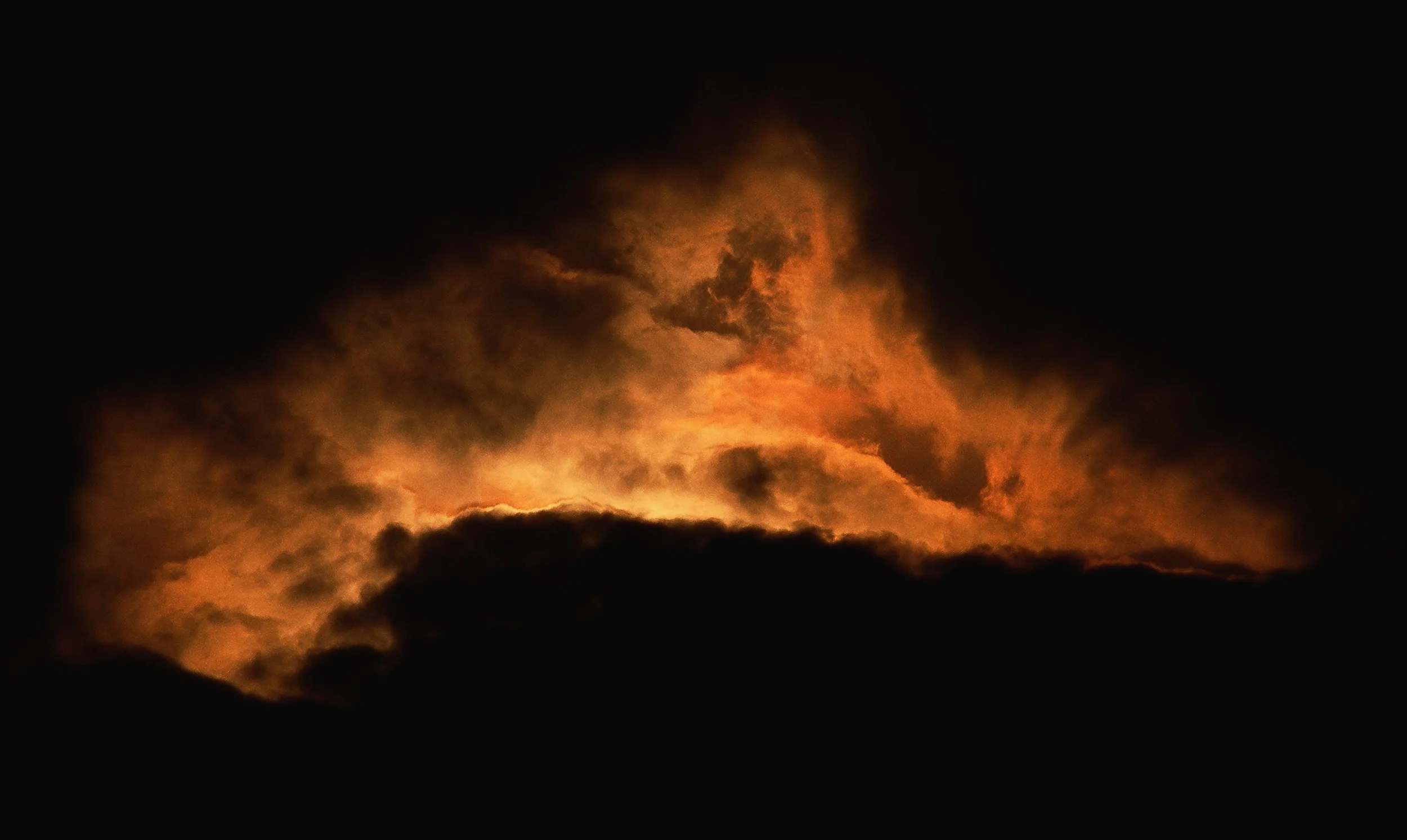 A dark night sky with orange clouds illuminated by a fire or explosion.