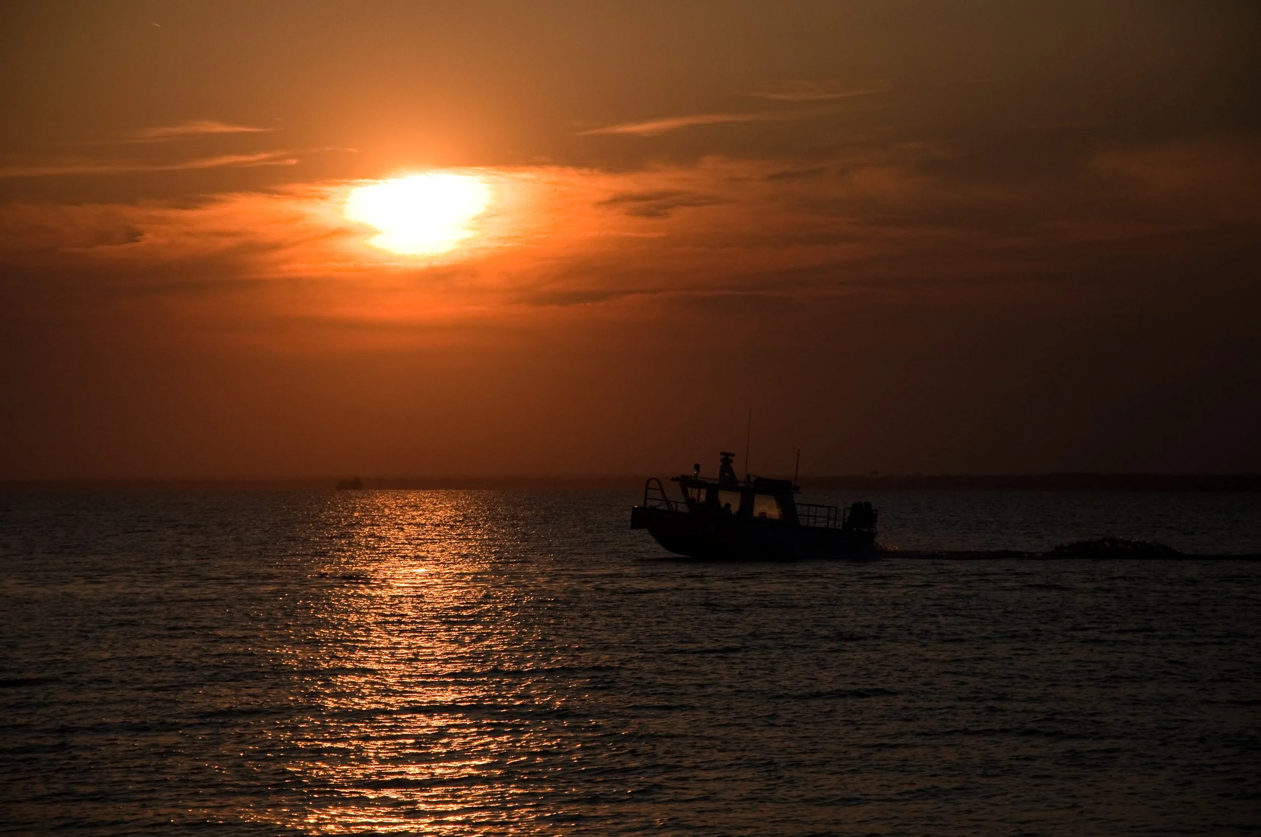 Sunset over the ocean with a silhouetted boat moving across the water.