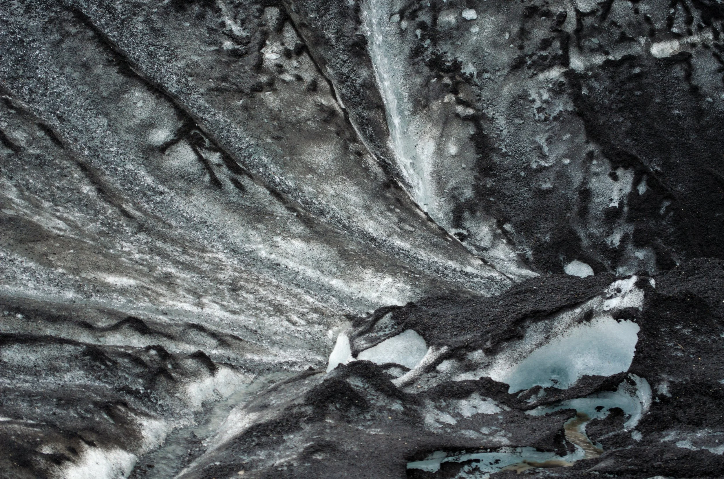 Close-up of volcanic rock formations with black and gray textures and some patches of snow or ice.