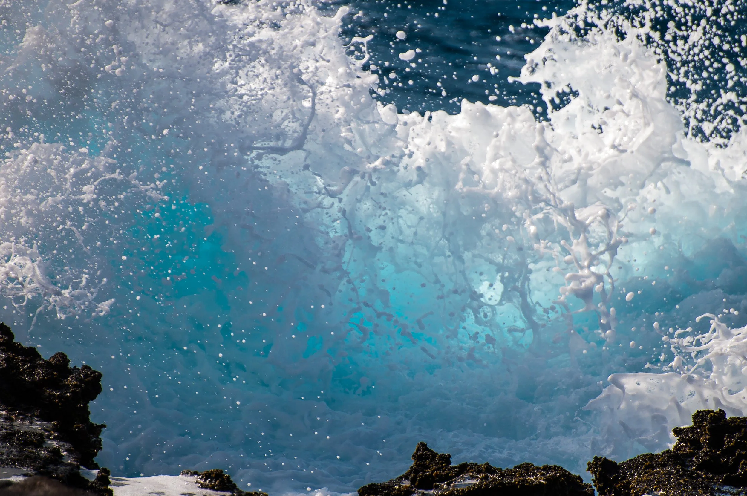 Ocean wave crashing against rocks with white foam and spray