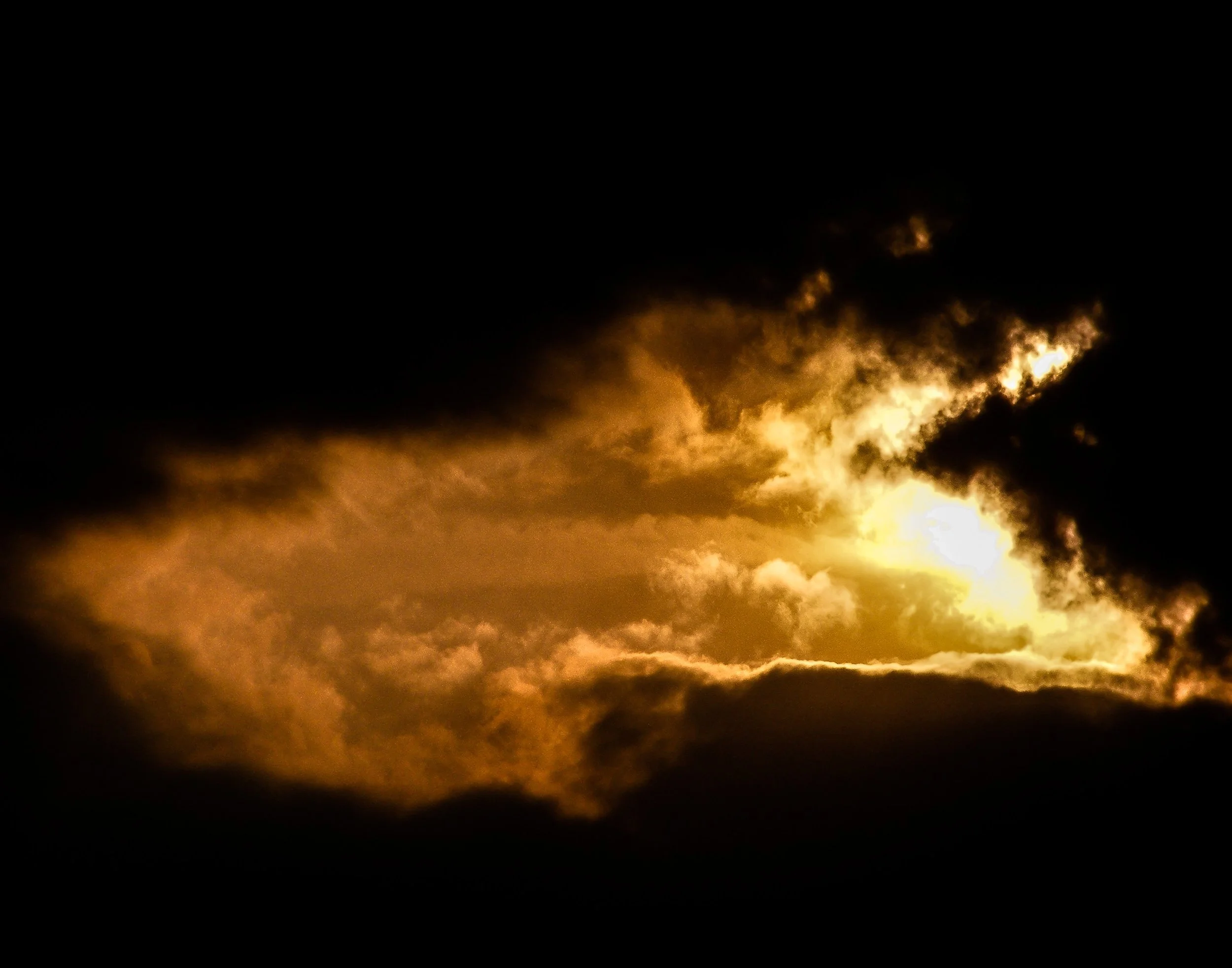 A dramatic sky with dark clouds and a bright opening where sunlight is breaking through